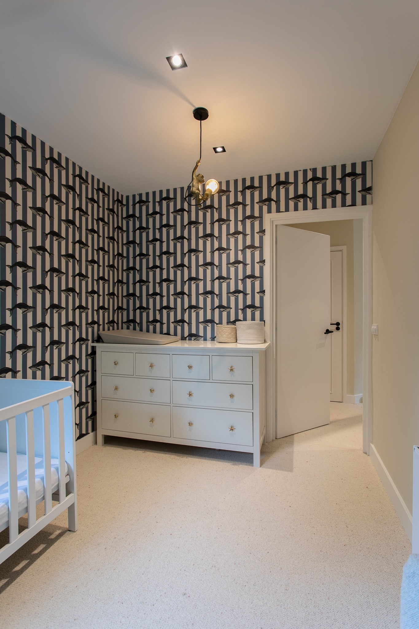 Babykamer met zwart-wit geometrisch behang, wit ledikant en zacht crèmekleurig tapijt.