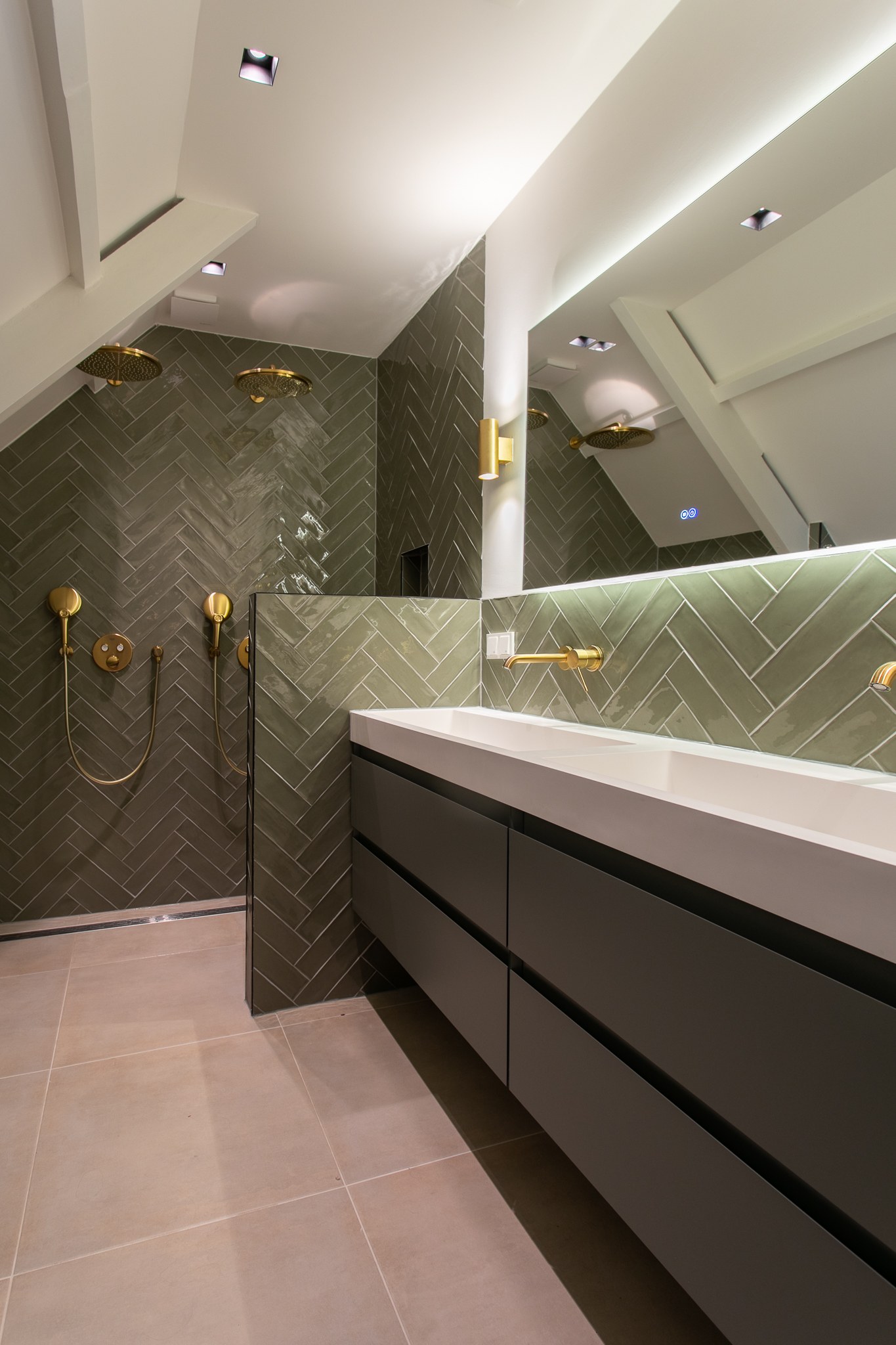 Moderne badkamer met donkergroene visgraattegels, matzwart wastafelmeubel, brede spiegel met indirect licht, messing kranen en lichte tegelvloer.