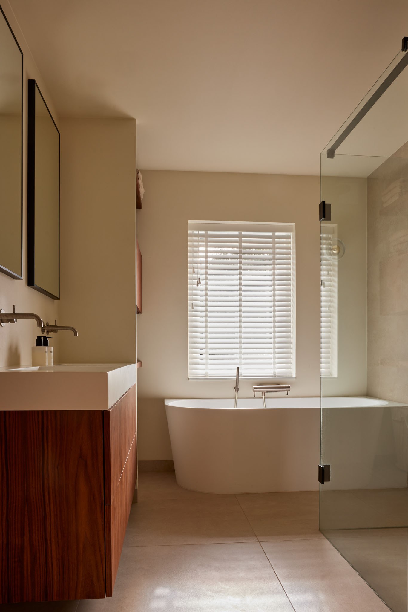 Luxe beige badkamer met vrijstaand bad, glazen inloopdouche en walnoot wastafelmeubel.