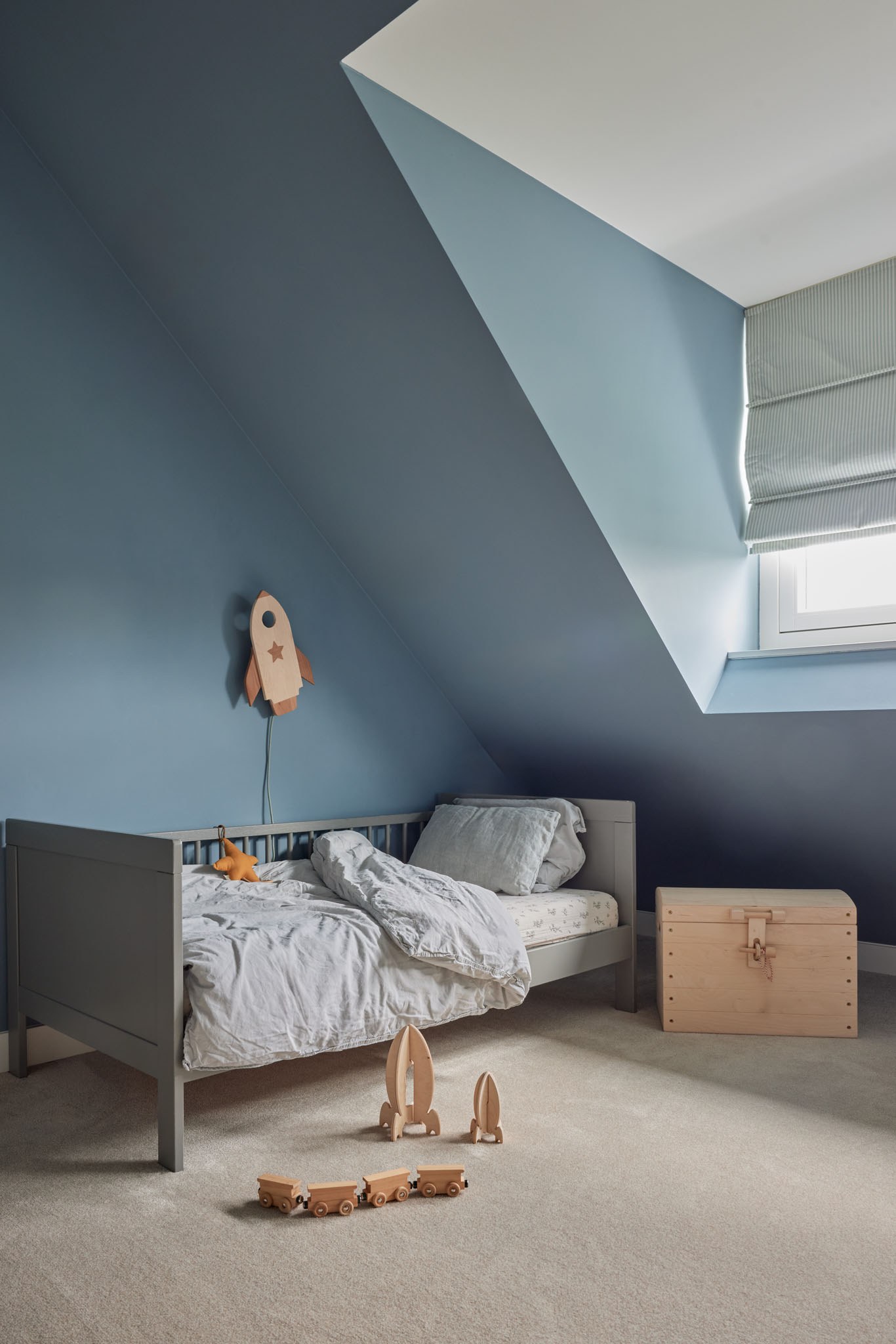 Kinderkamer met blauwe wanden en maatwerk onder een schuin dak.