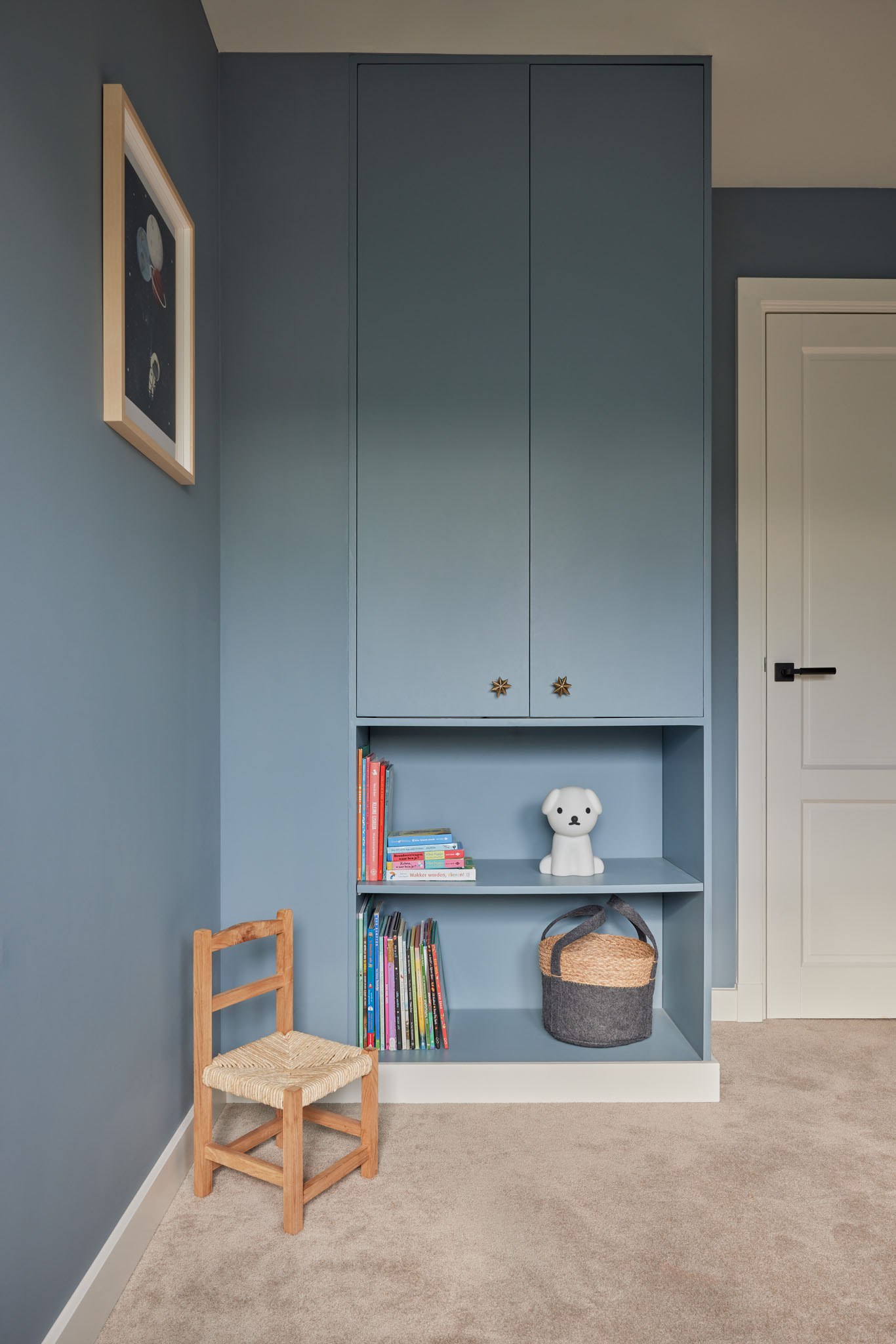 Blauwe ingebouwde kledingkast en boekennis in een kinderkamer onder schuin dak.