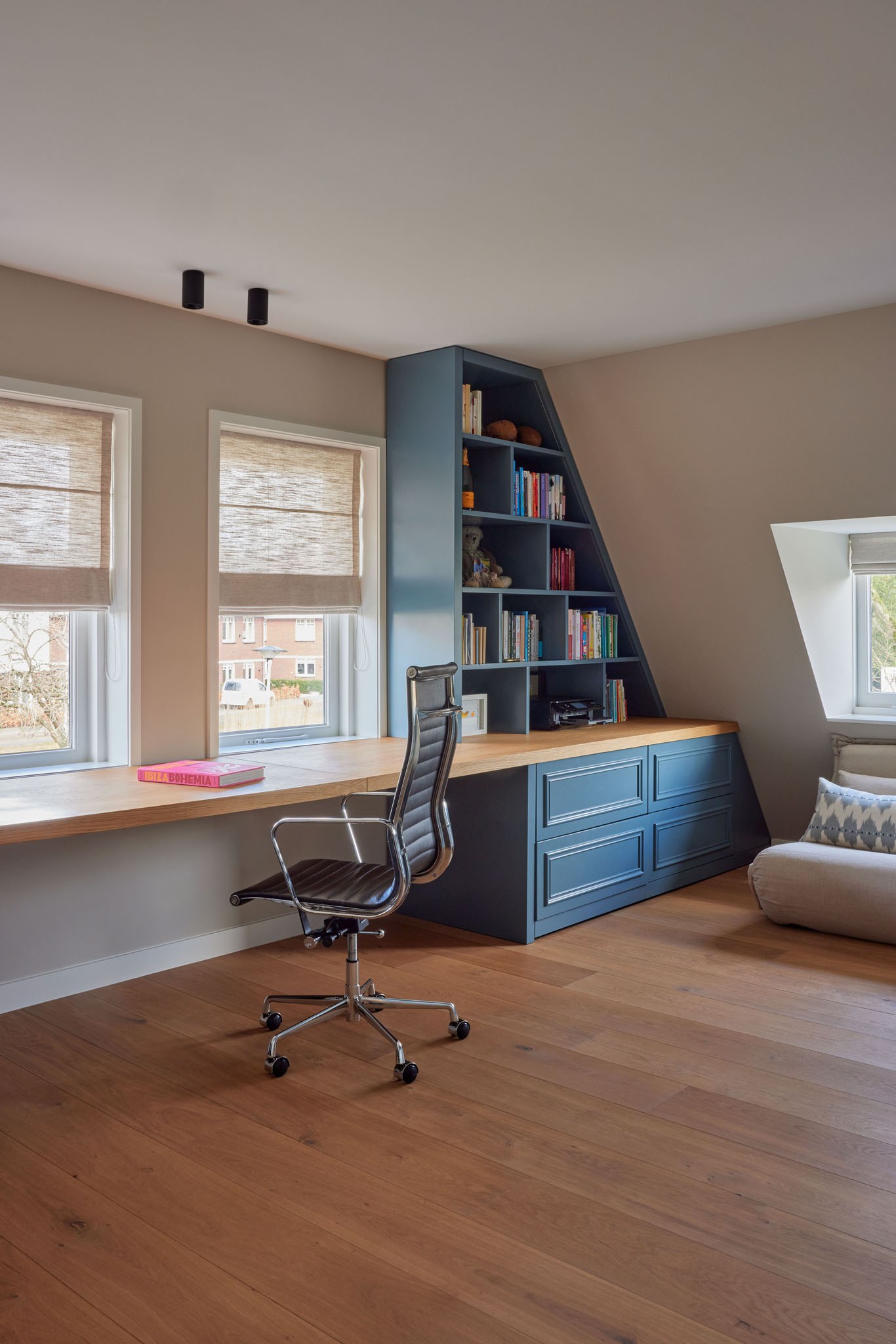 Werkkamer met blauwe maatwerkkasten en ingebouwd bureau onder een schuin dak.