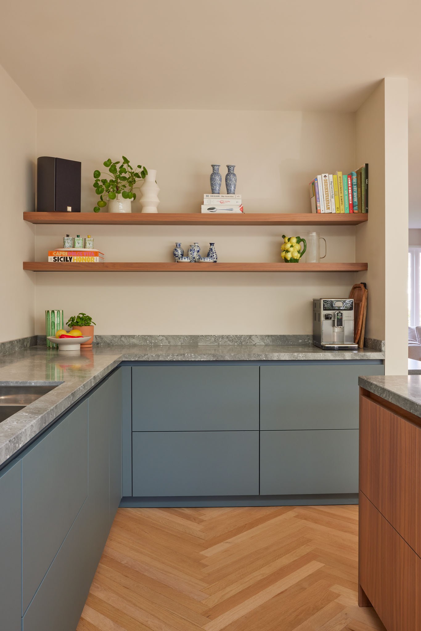 Keuken met blauwgrijze onderkasten, open walnoot wandplanken en visgraatvloer.