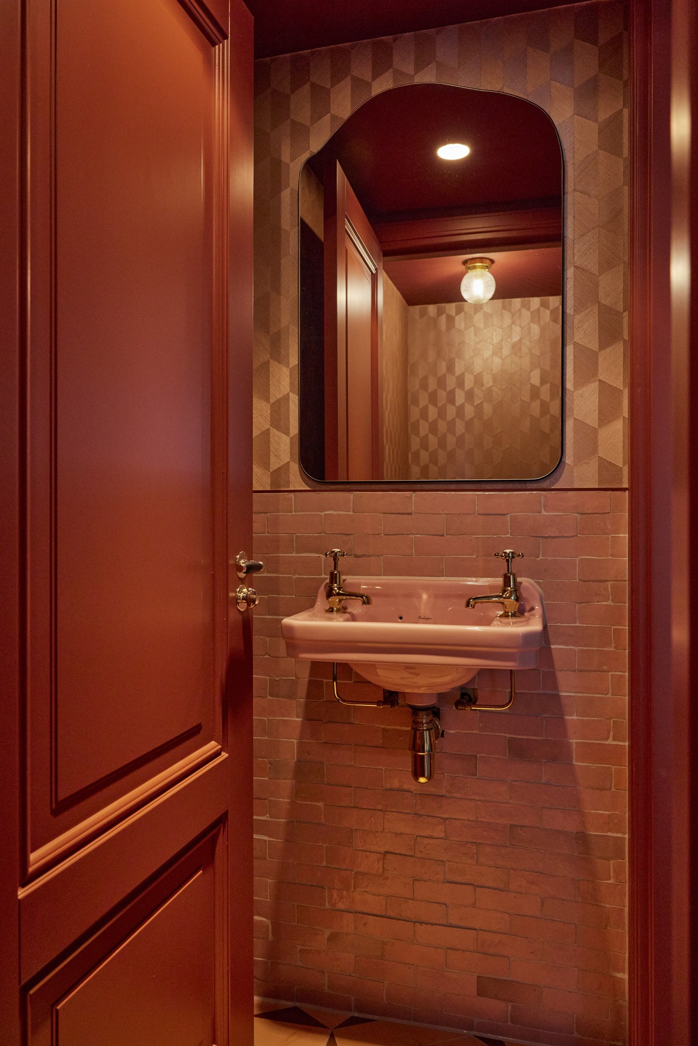 Compacte toiletruimte met diepe bordeaux wanden, roze tegels en fontein en gebogen spiegel.