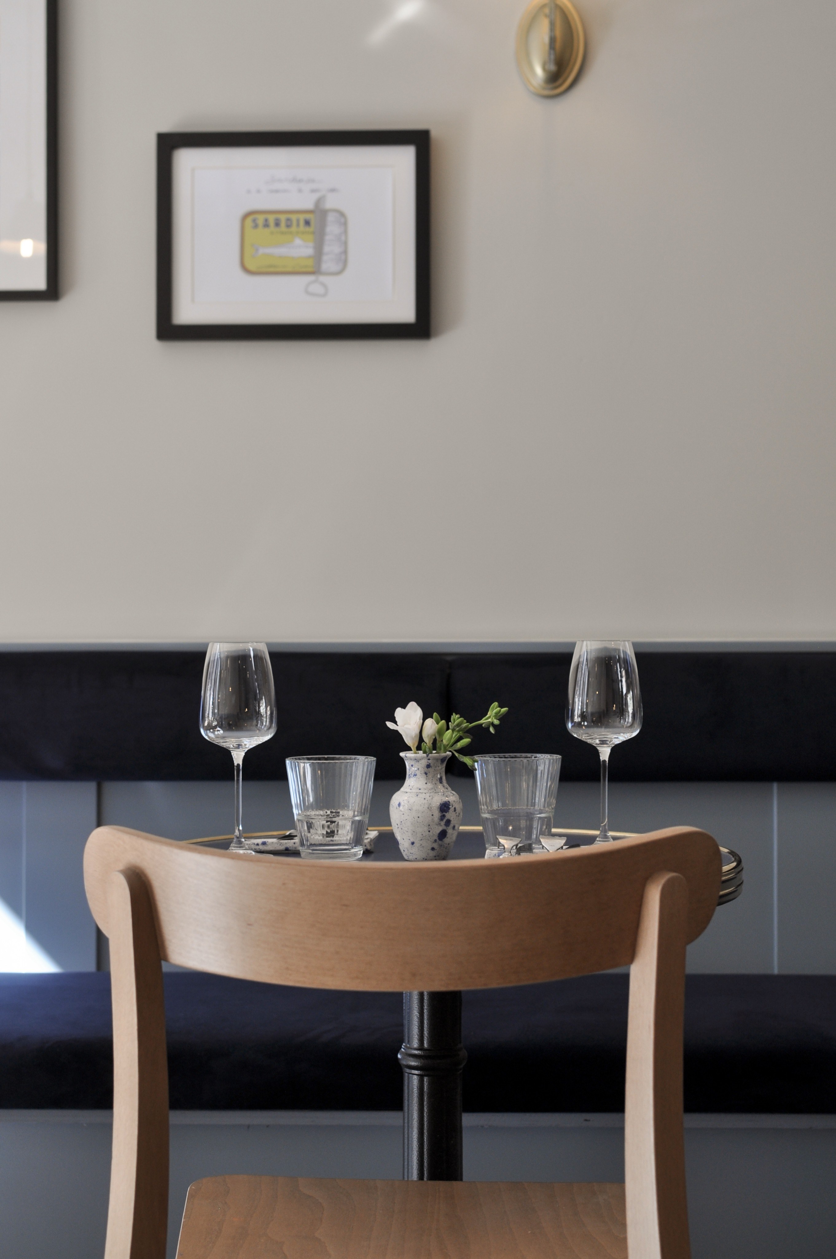 Gedekte ronde cafétafel met houten stoel en donkerblauwe gepaneelde wandbank.
