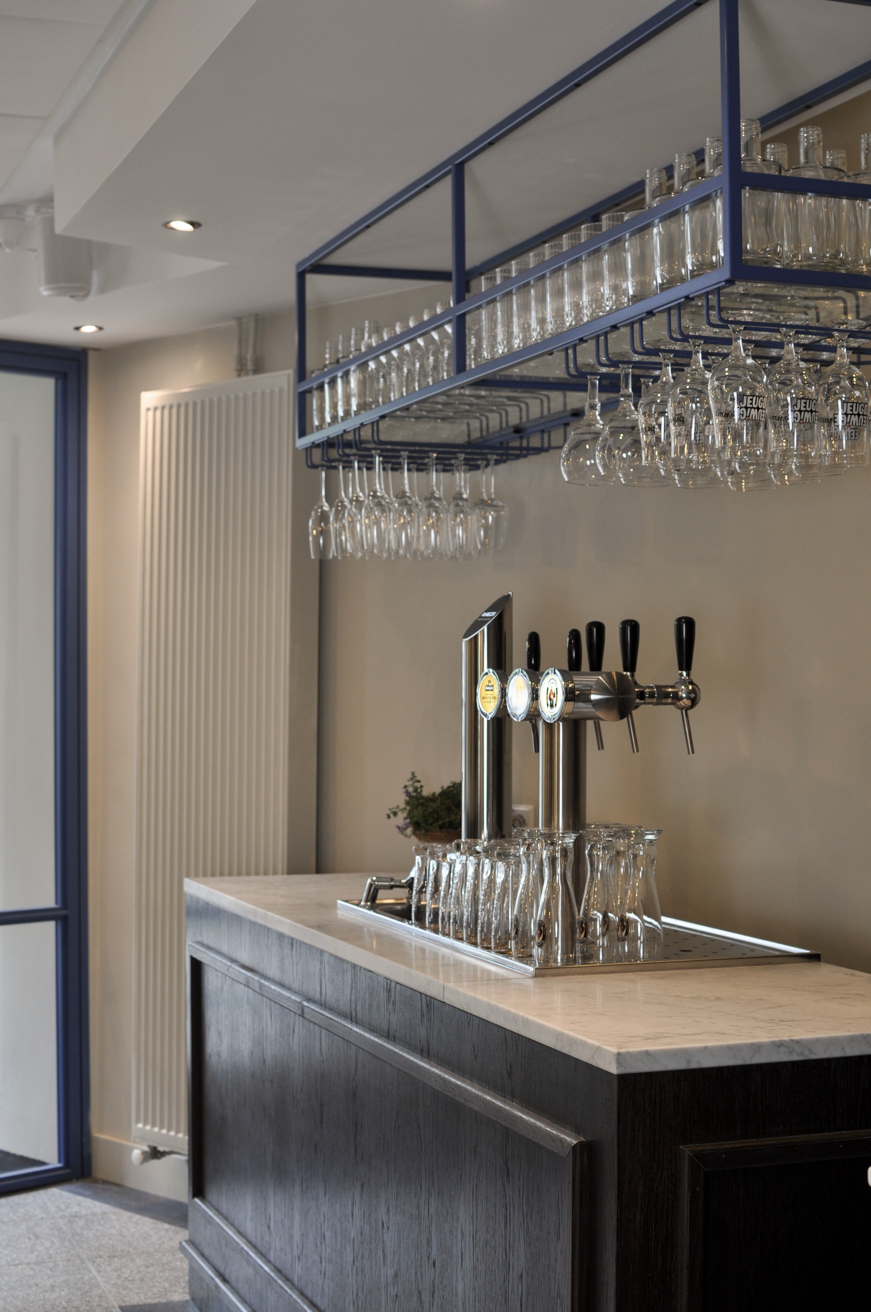 Maatwerk cafébar met donker houten front, licht stenen blad, biertaps en zwart metalen glazenrek.