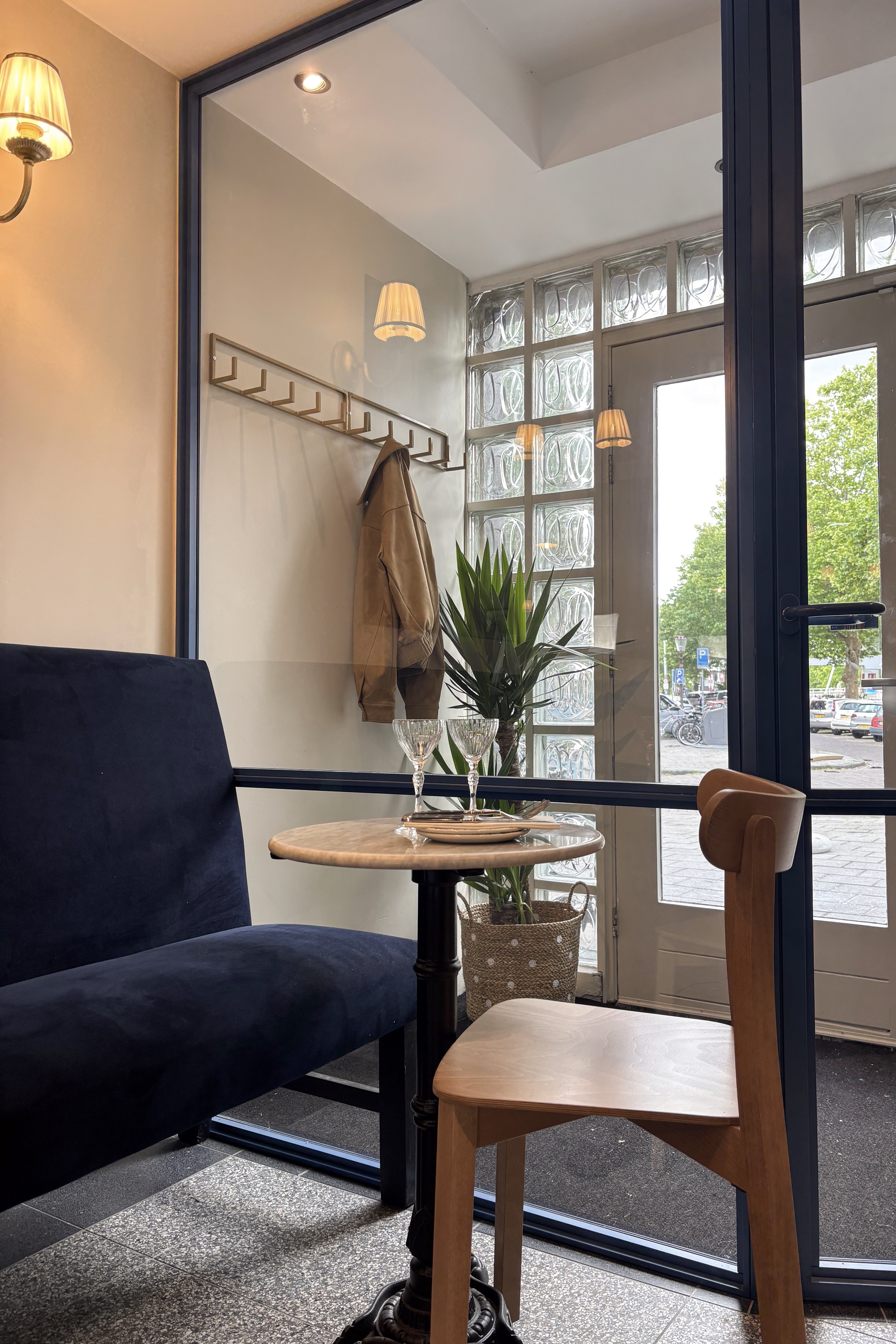Compacte zitplek met donkerblauwe bank, houten stoel en zwarte stalen glaswand bij de entree.