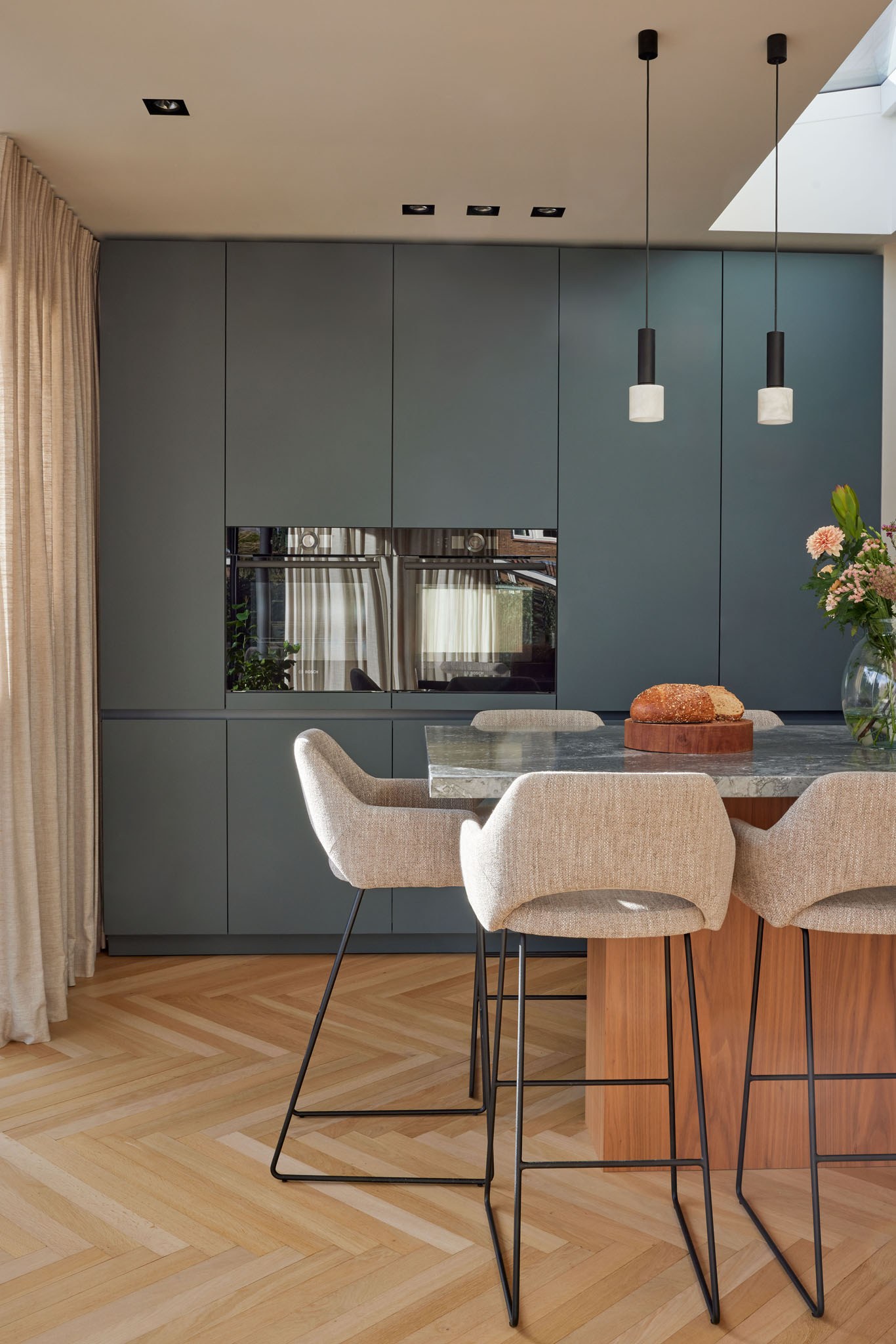 Keuken met donker blauwgrijze kastenwand, walnoot kookeiland en glazen hanglampen.