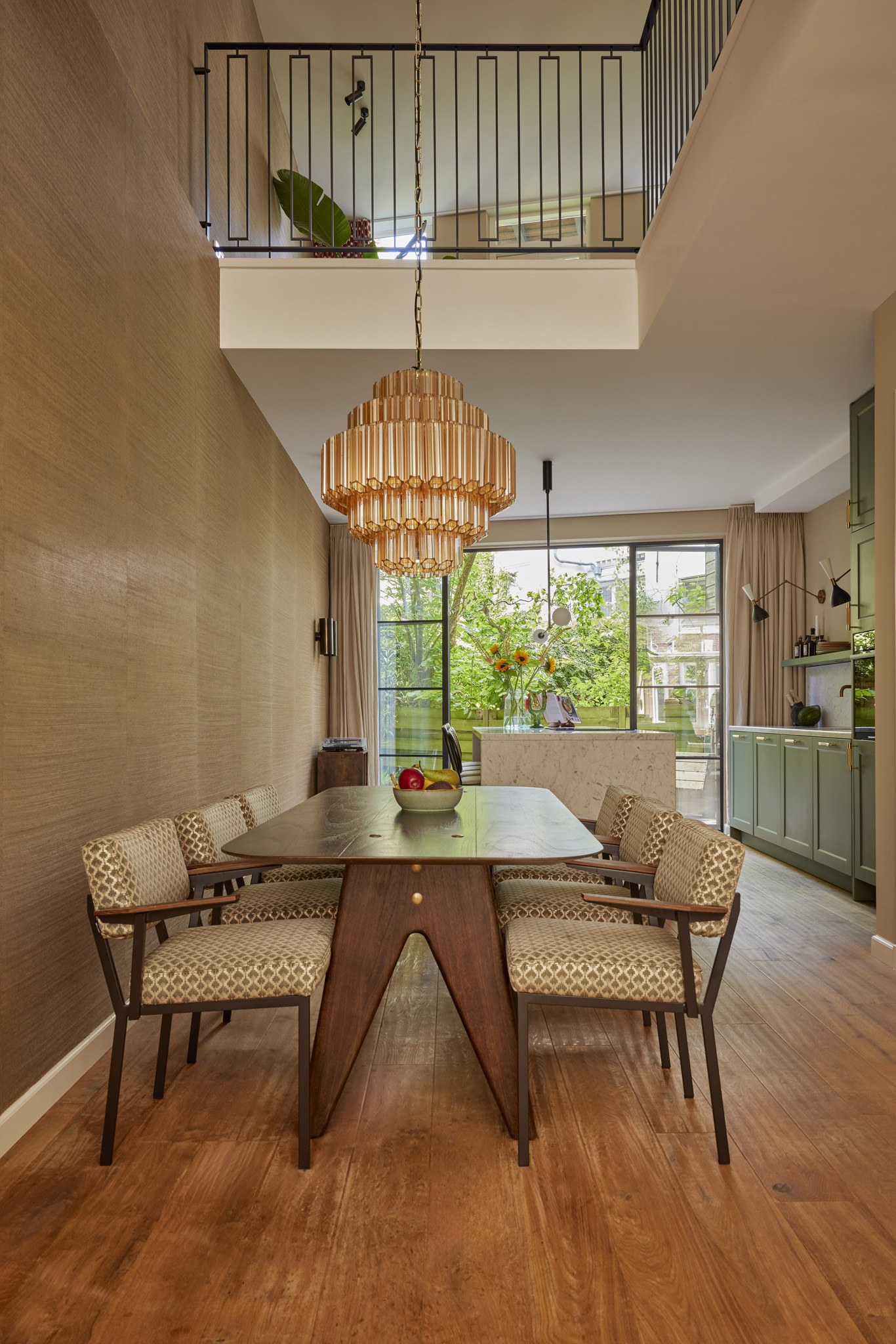 Warme eetkamer met houten tafel, natuurlijke wandtextuur, rotan hanglamp en groene keuken.