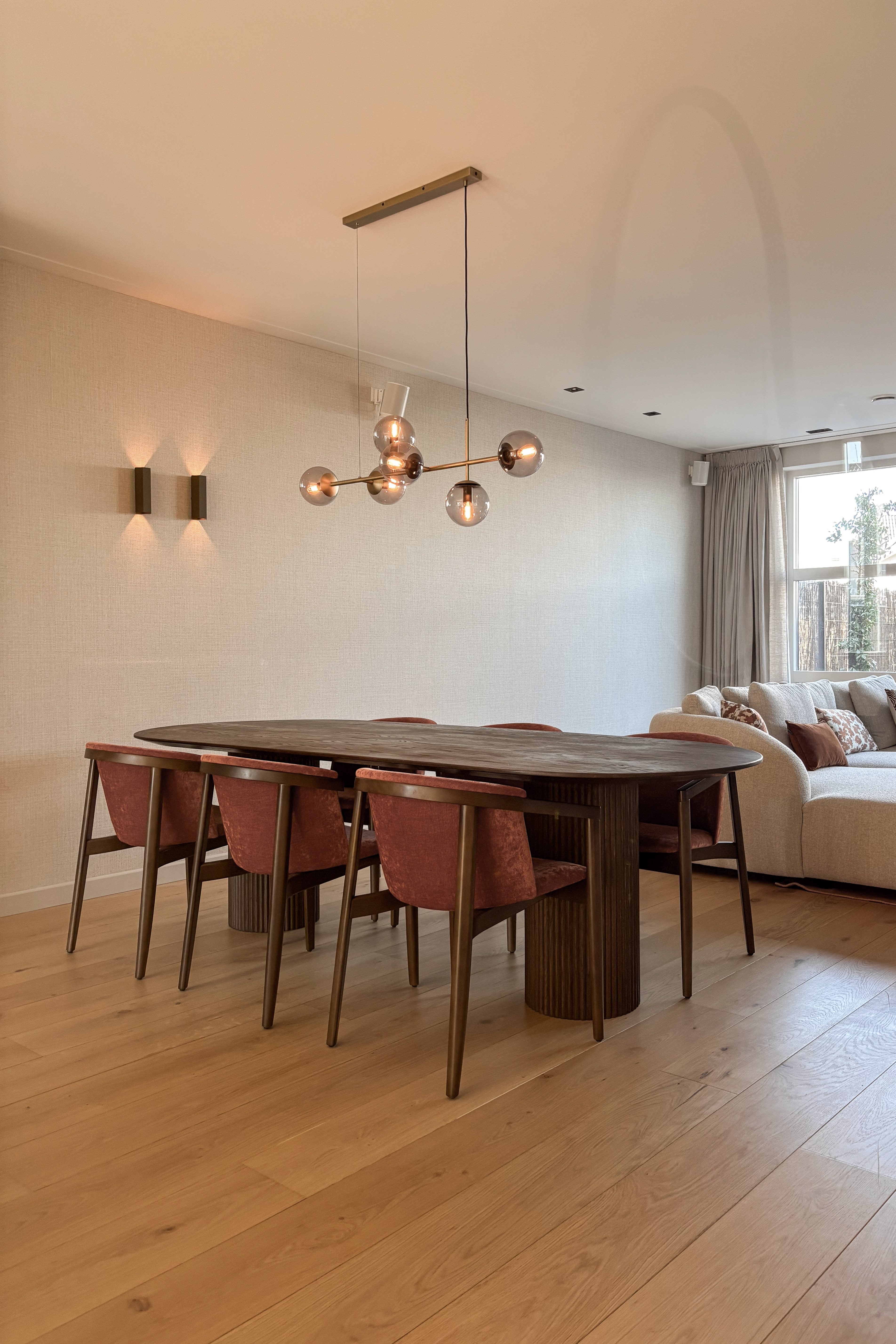 Eetkamer met donkere houten tafel, roestkleurige stoelen en glazen bolhanglampen.