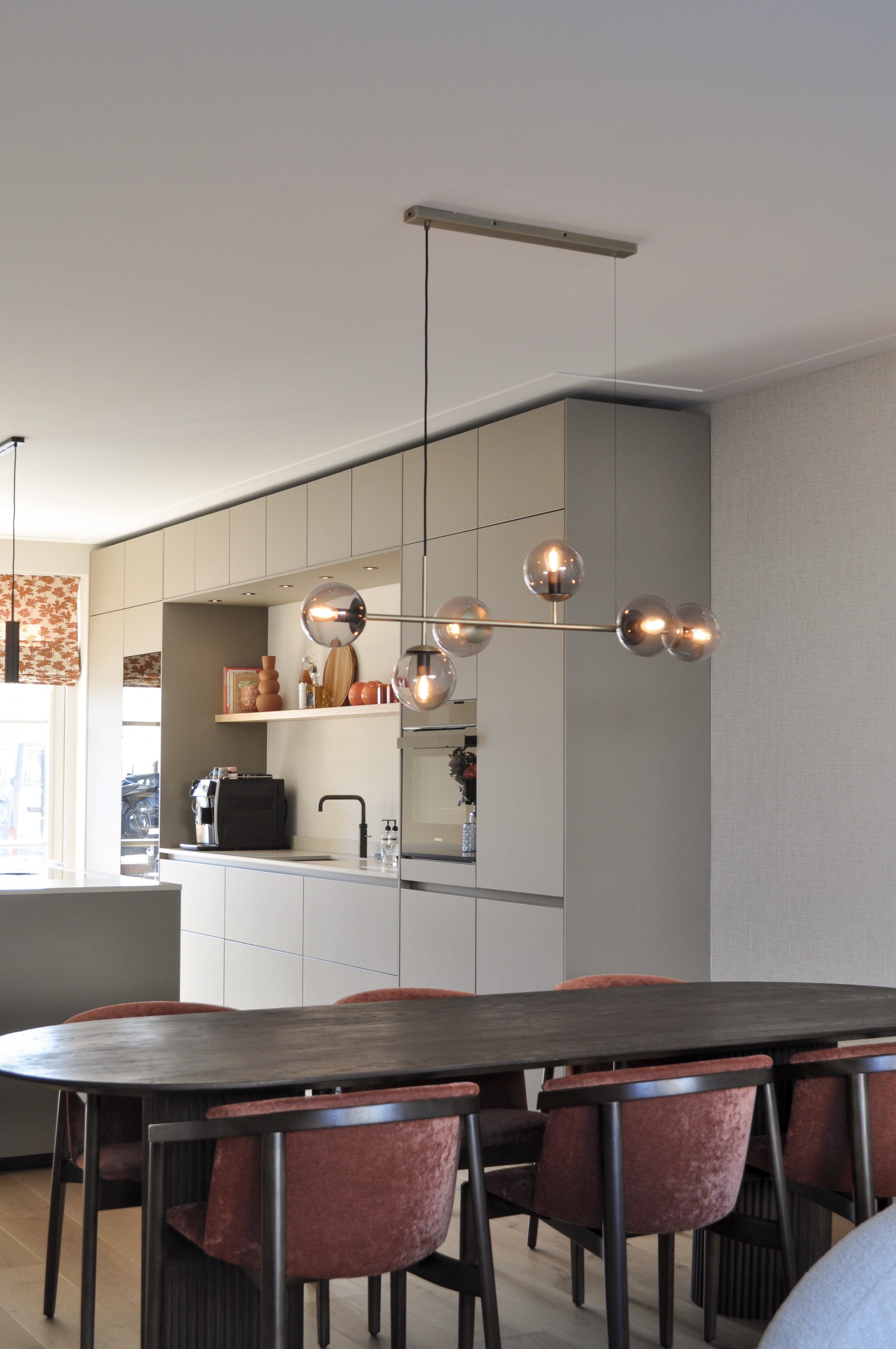 Eetkamer met roestkleurige stoelen, glazen bolverlichting en zicht op taupe keuken.