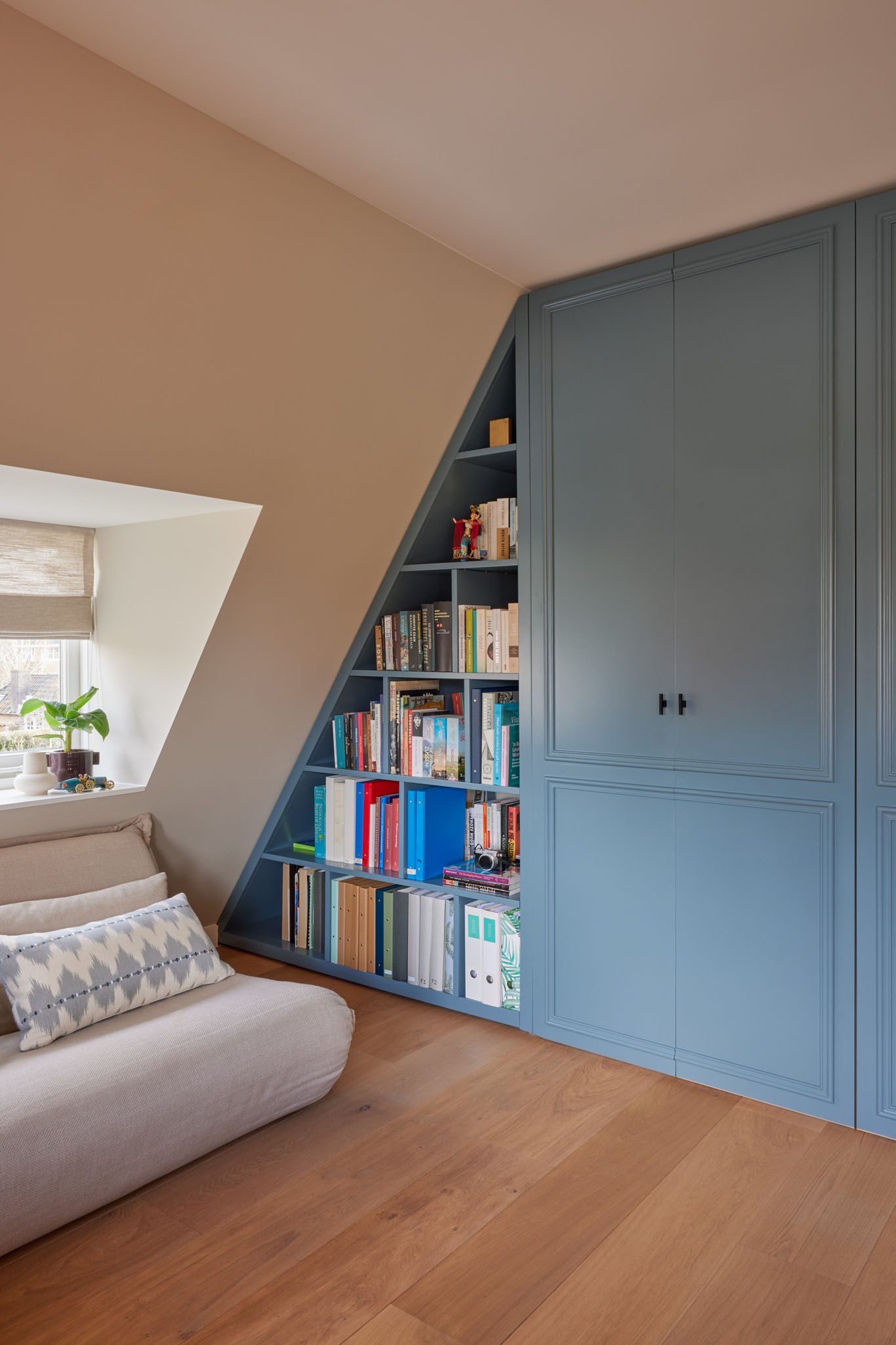Blauwe ingebouwde boekenkast en garderobe onder een schuine kap.