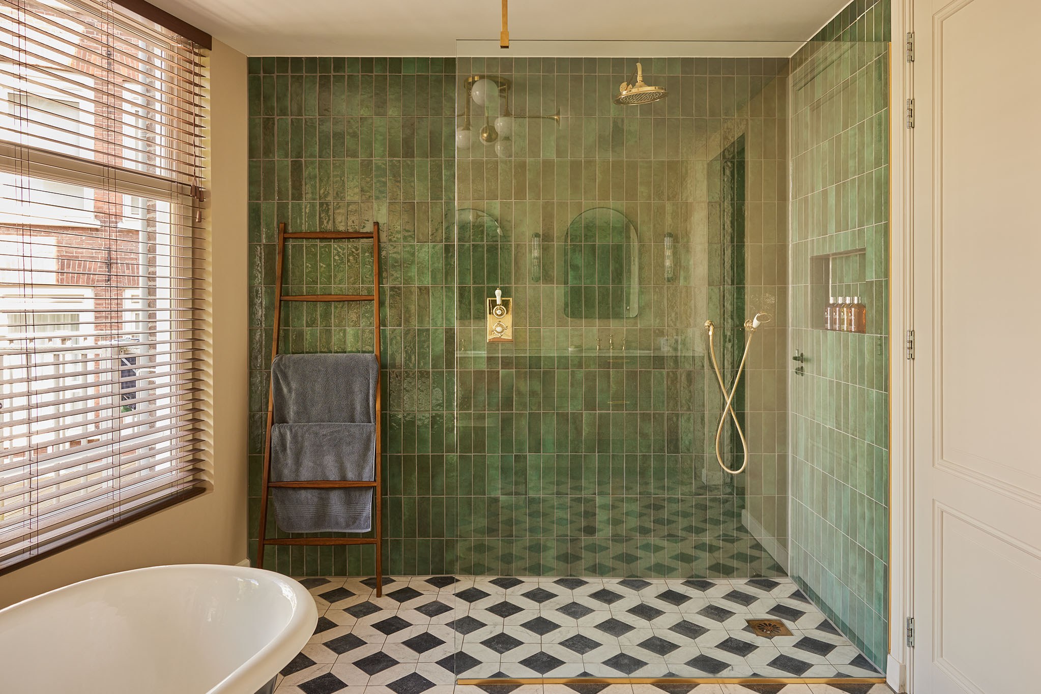 Badkamer met groene tegels, zwart-witte dambordvloer, bad en messing kranen.