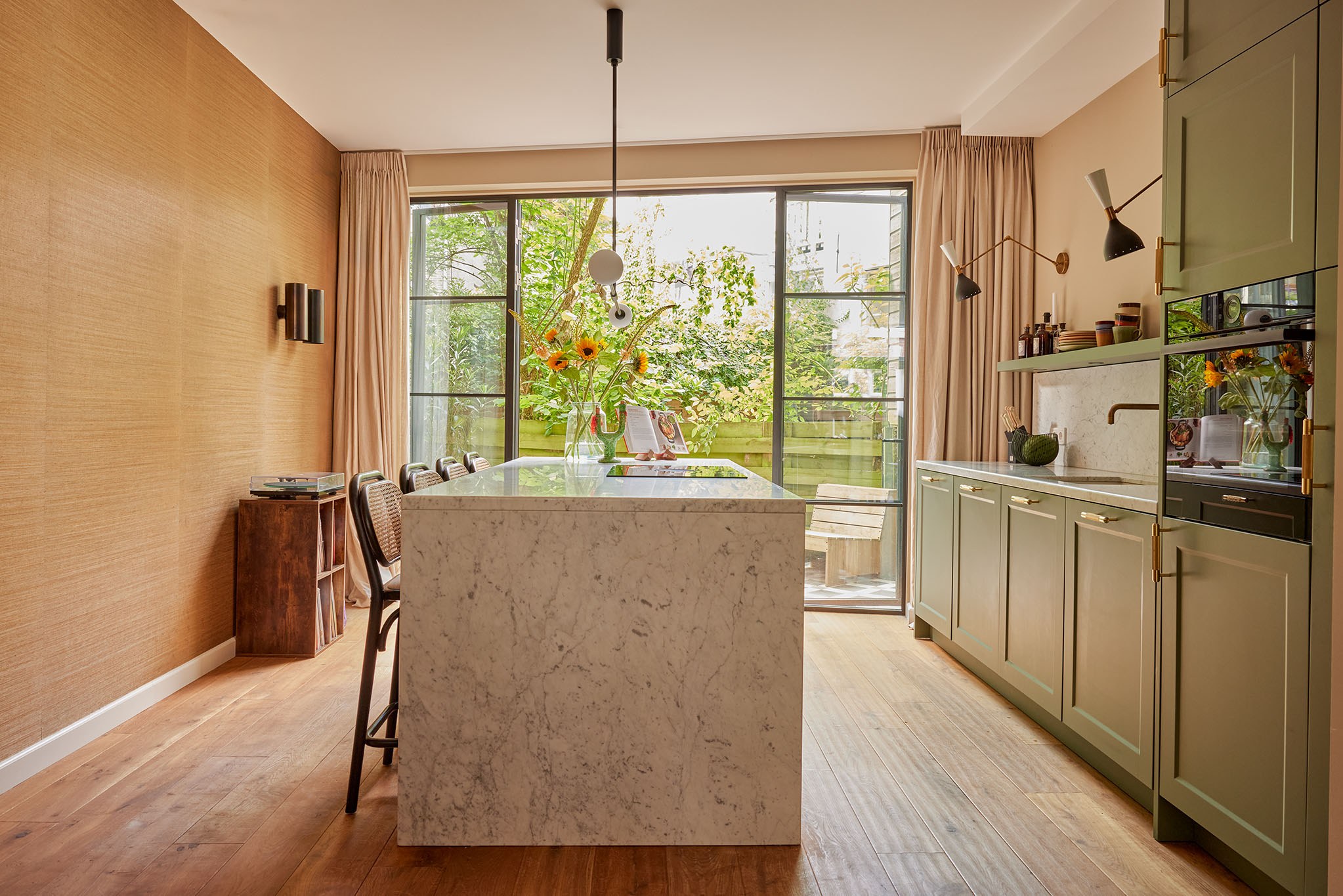 Luxe groene shakerkeuken met wit marmeren watervaleiland, grasweefselwand en grote glazen deuren.