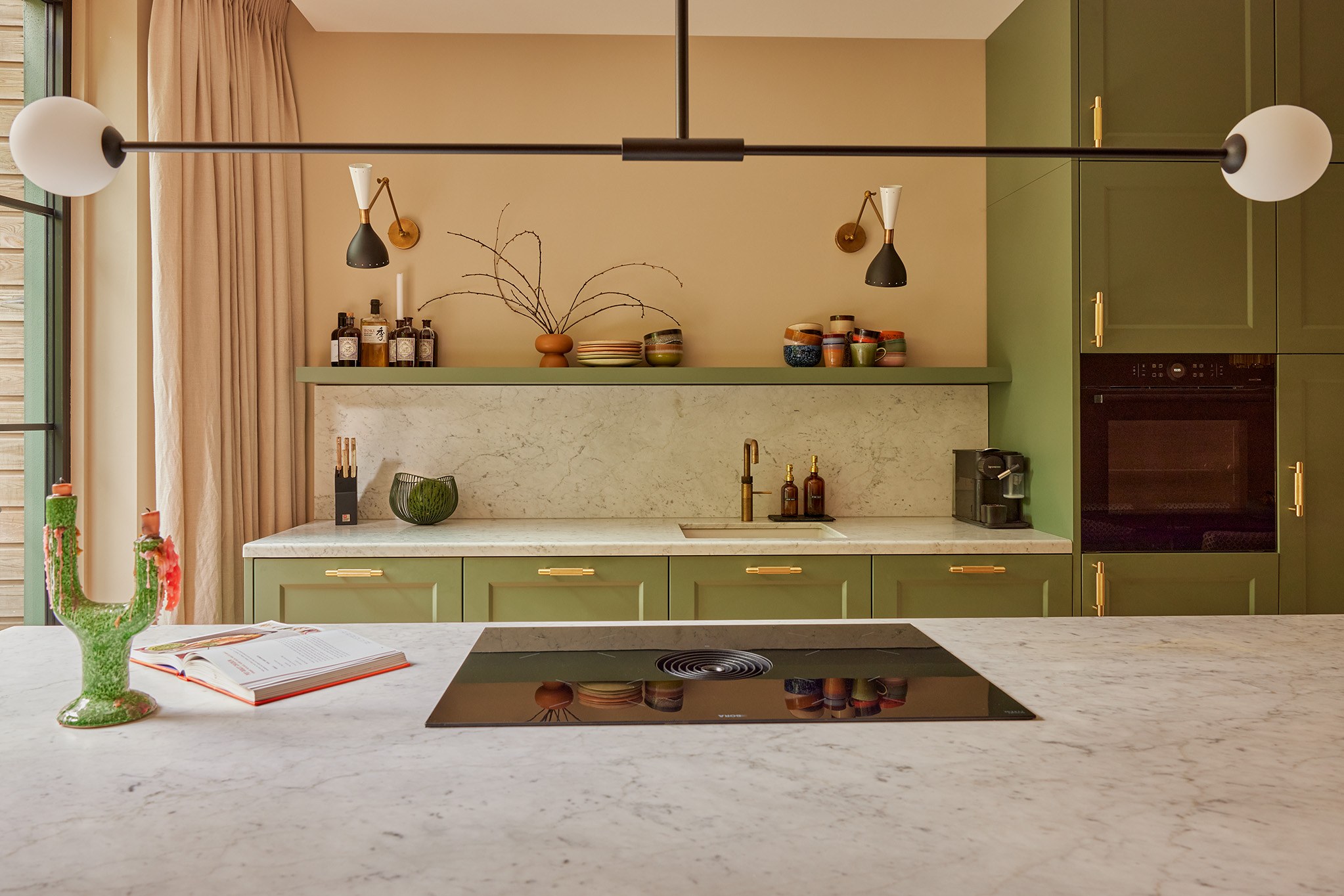 Front van groene shakerkeuken met wit marmeren werkblad en achterwand en messing details.