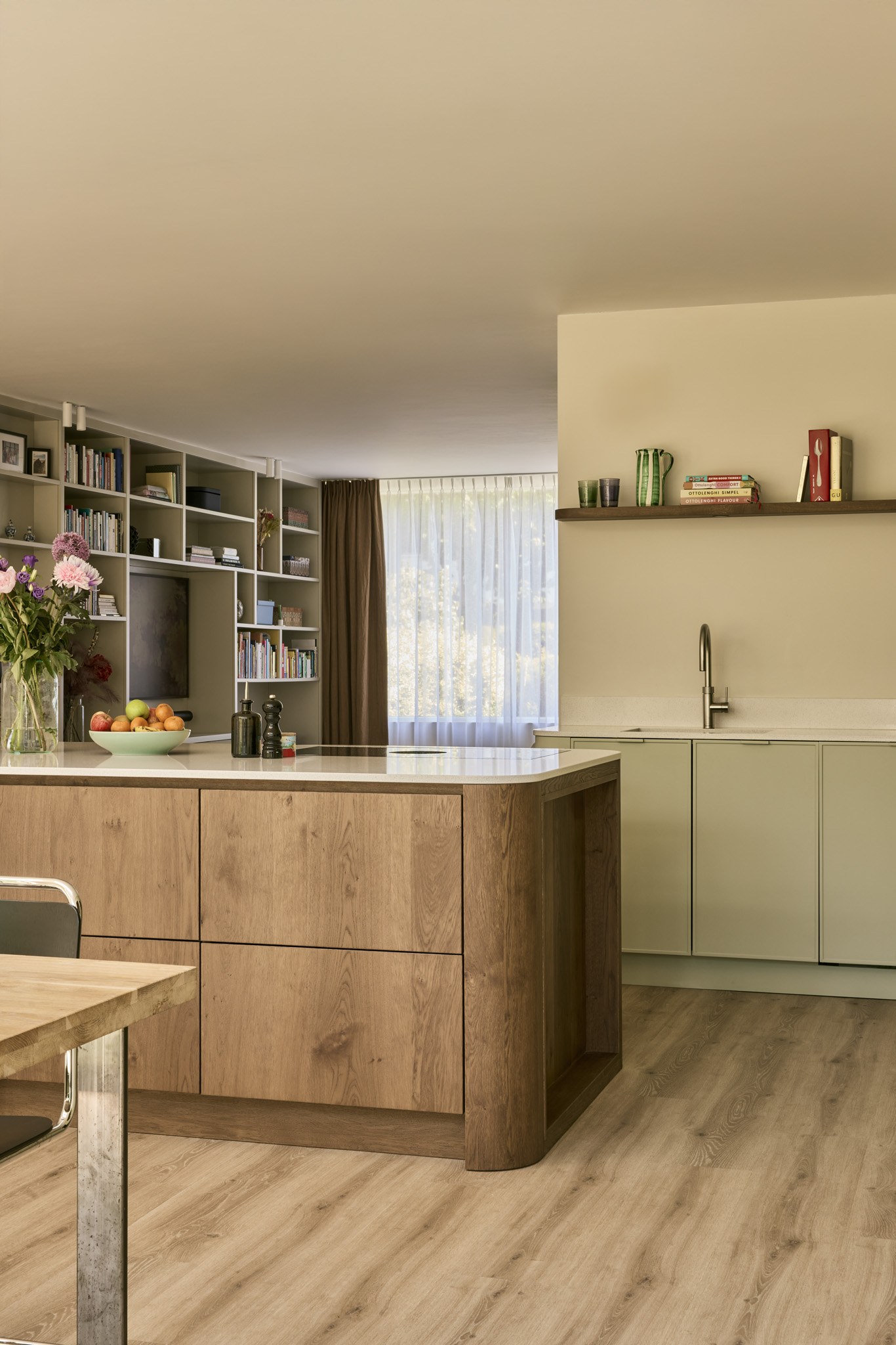Verticale opname van saliegroene maatwerkkeuken met eiken eiland en licht werkblad.