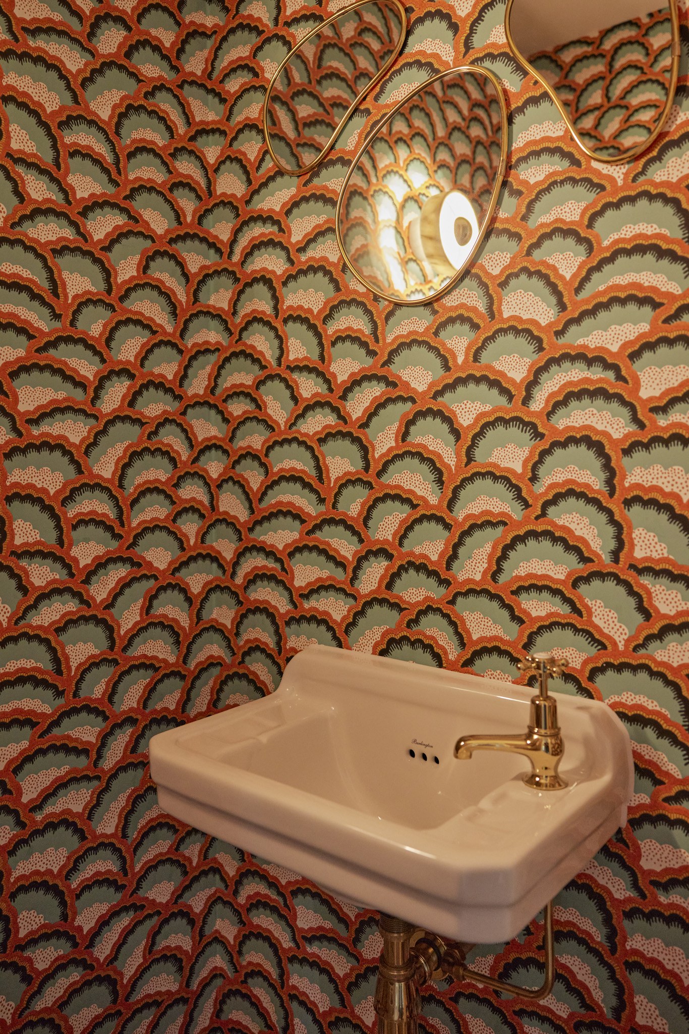 Wit fonteintje met messing kraan tegen oranje-groen geschulpt behang.