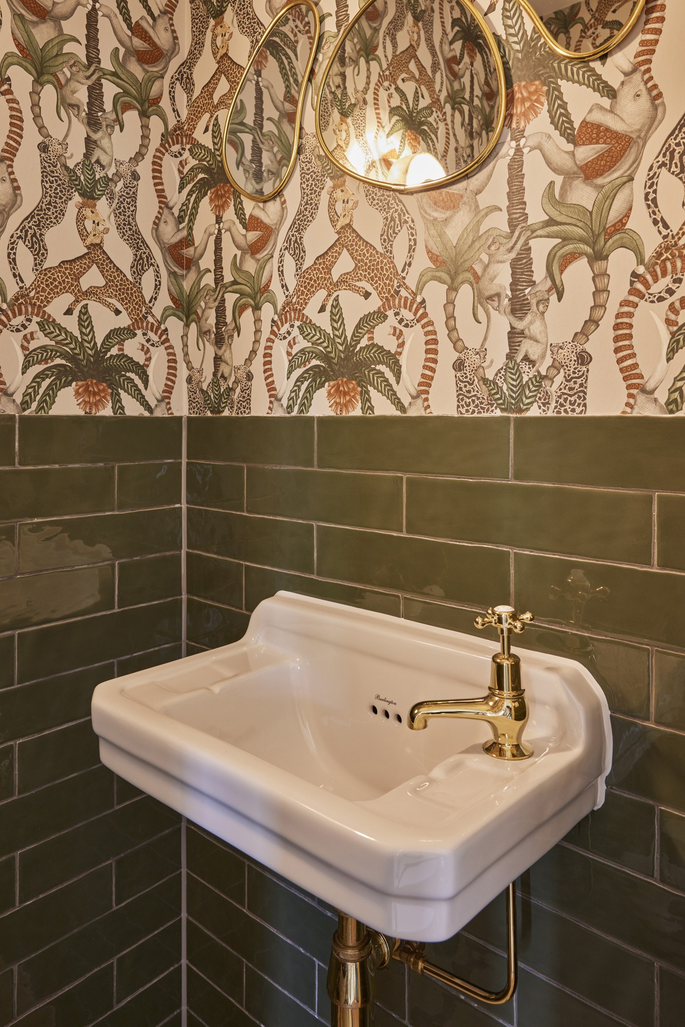 Wit fonteintje met messing kraan bij groene tegels en botanisch dierenbehang.