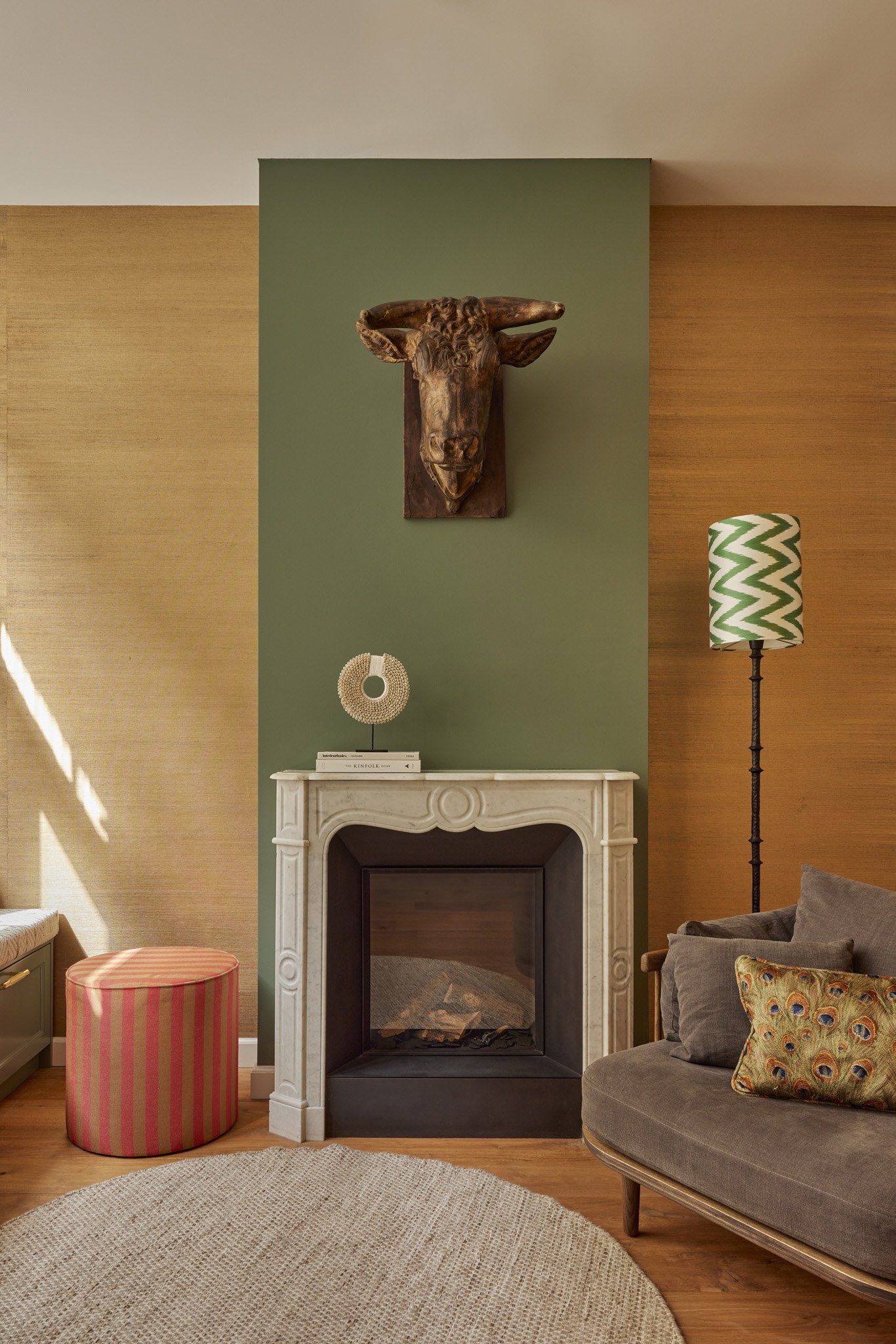 Detail van een haard tegen olijfgroene wand met sculpturale decoratie.