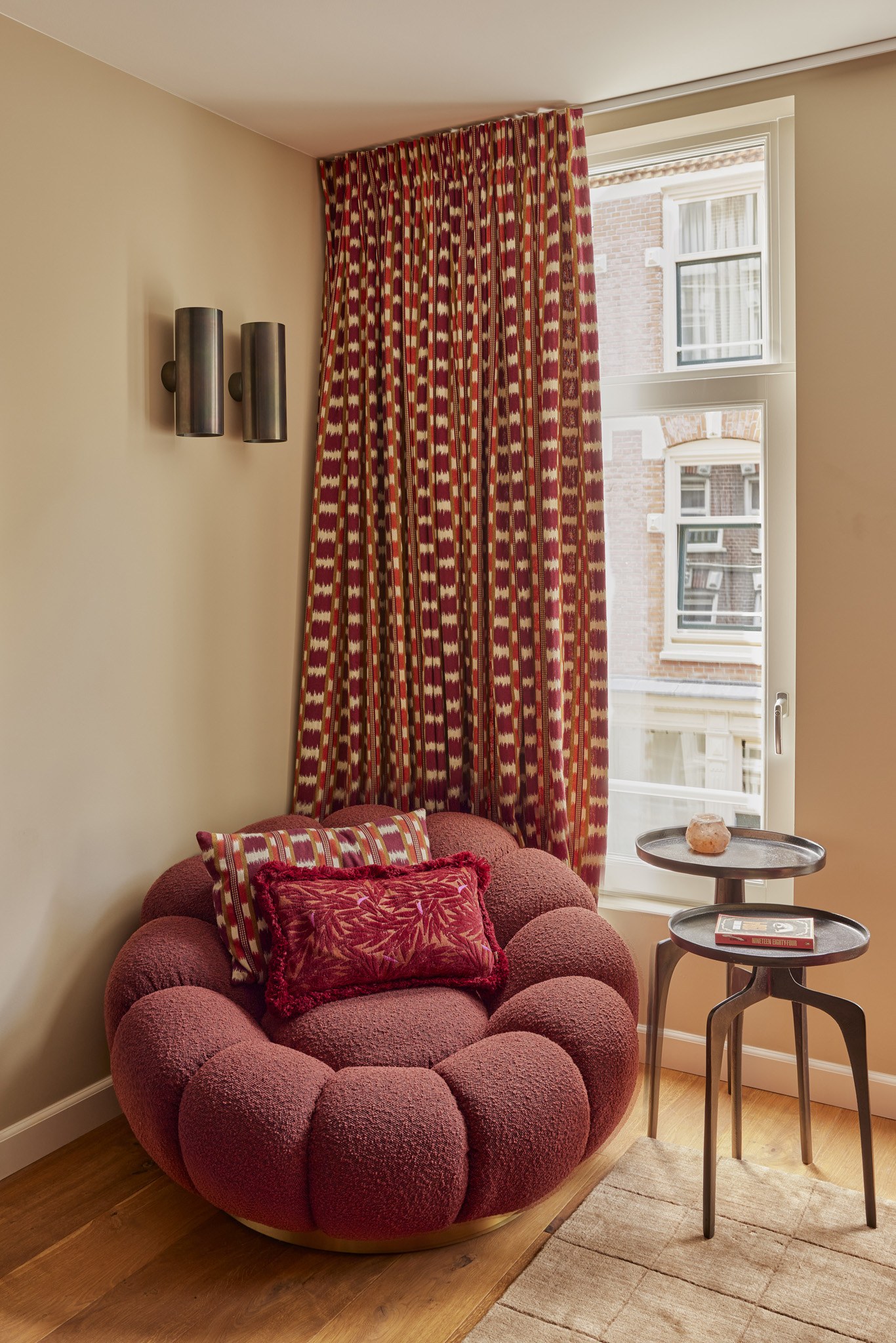 Sculpturale poederroze fauteuil naast een rood patroon gordijn.