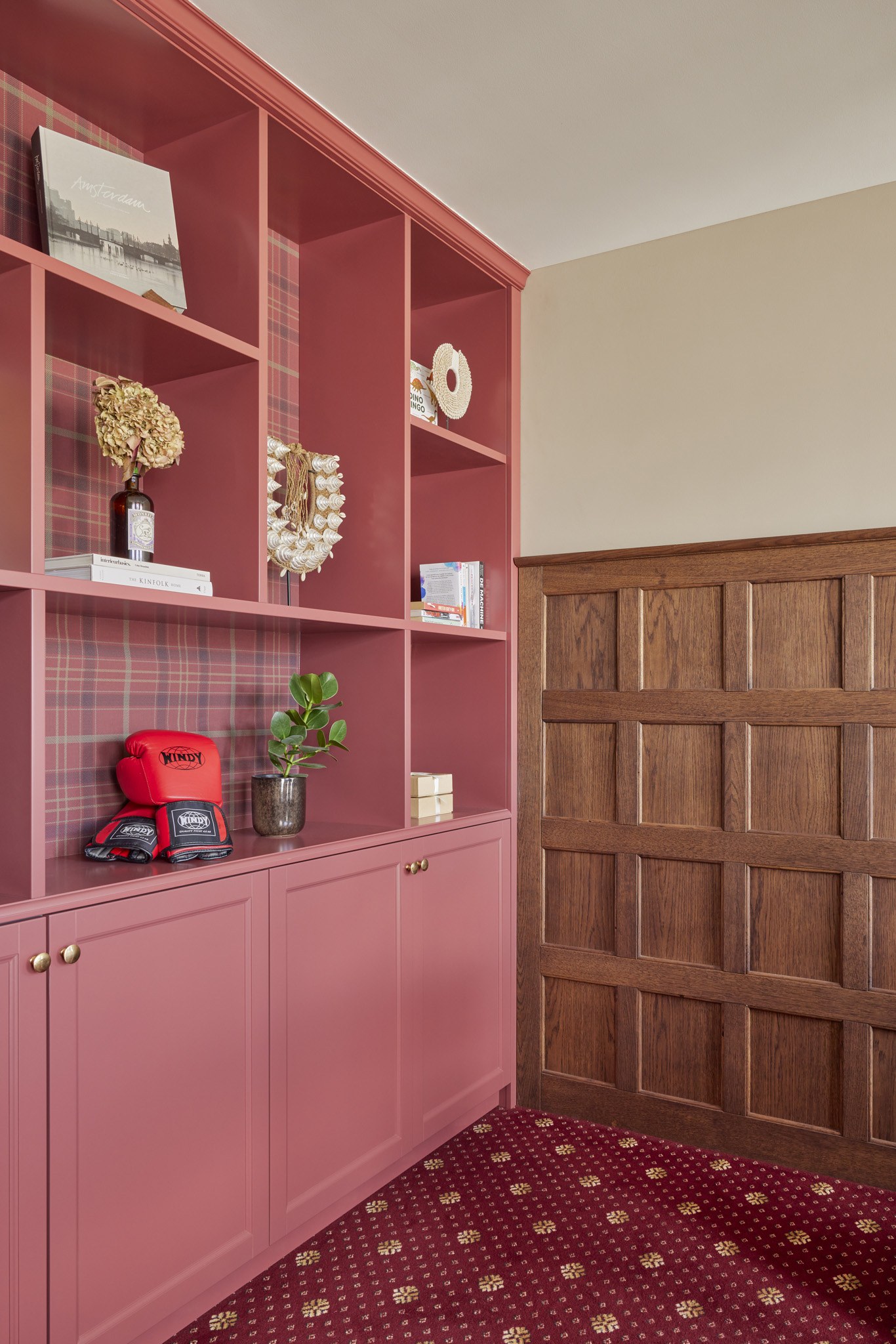 Roze ingebouwde kast met open vakken boven een bordeauxrode patroonvloer.