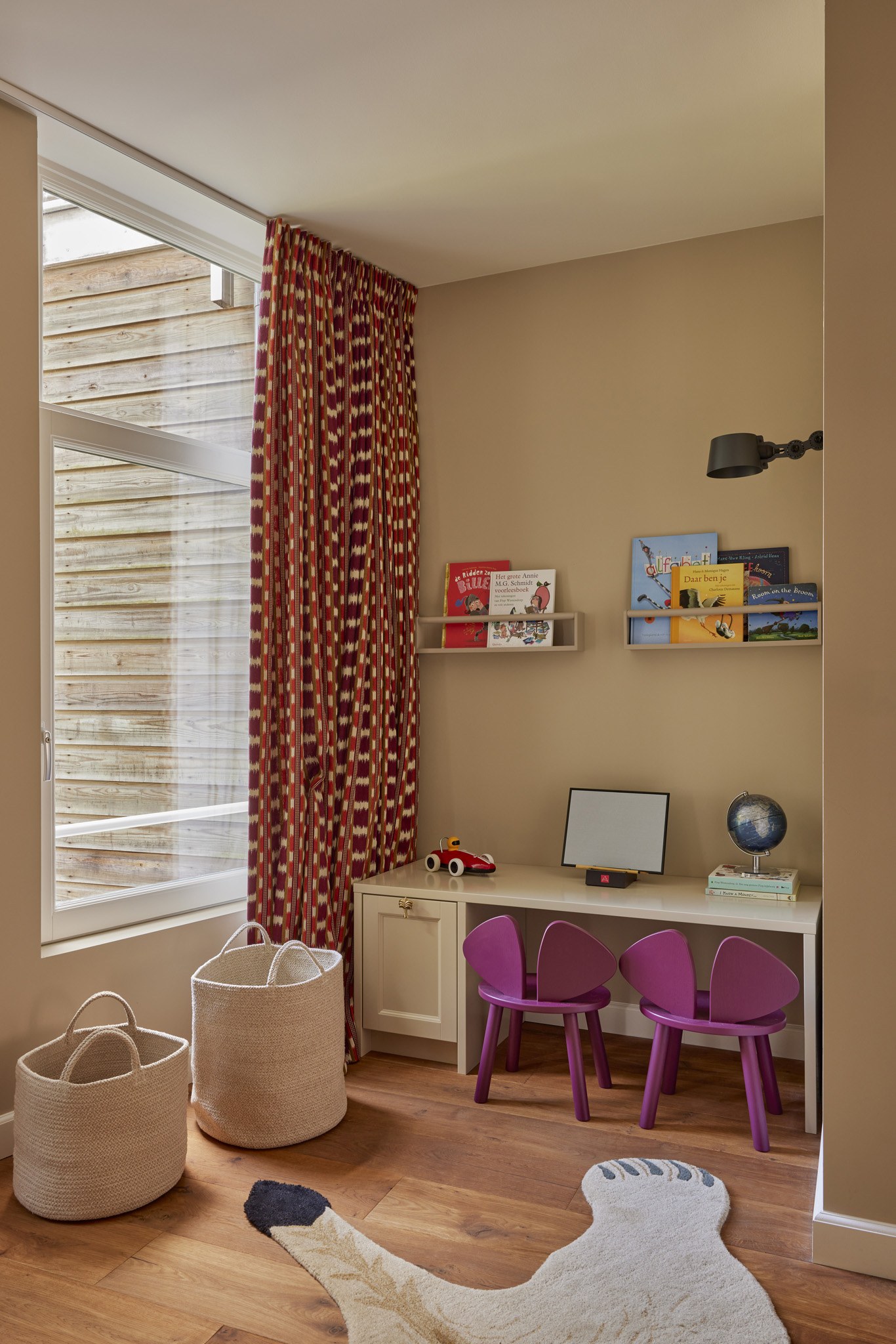 Kinderhoek met beige wanden, rode patroonstof en kleine paarse stoelen.
