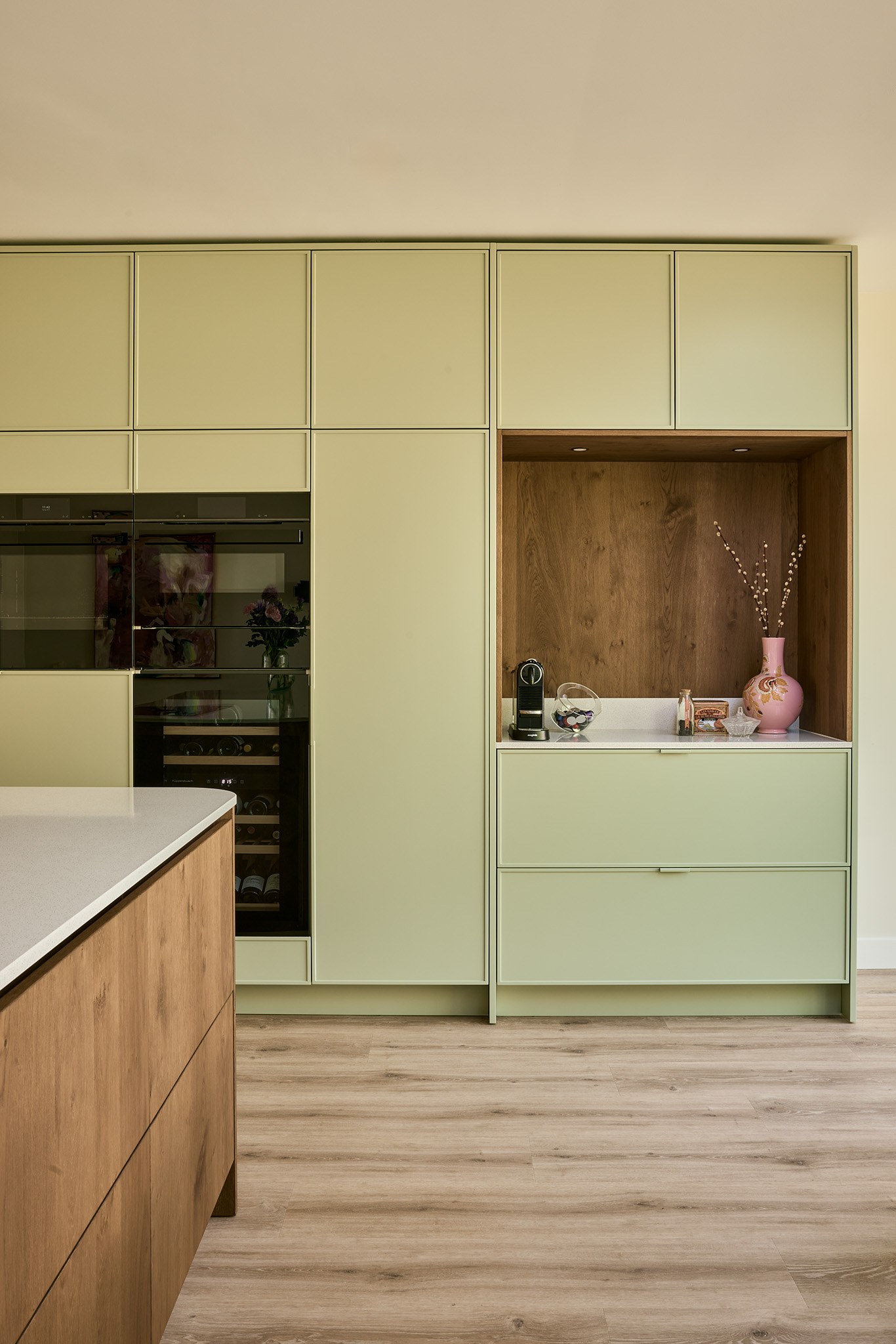 Lichte keuken met saliegroene hoge maatwerkkasten en warme eiken nis met werkblad.