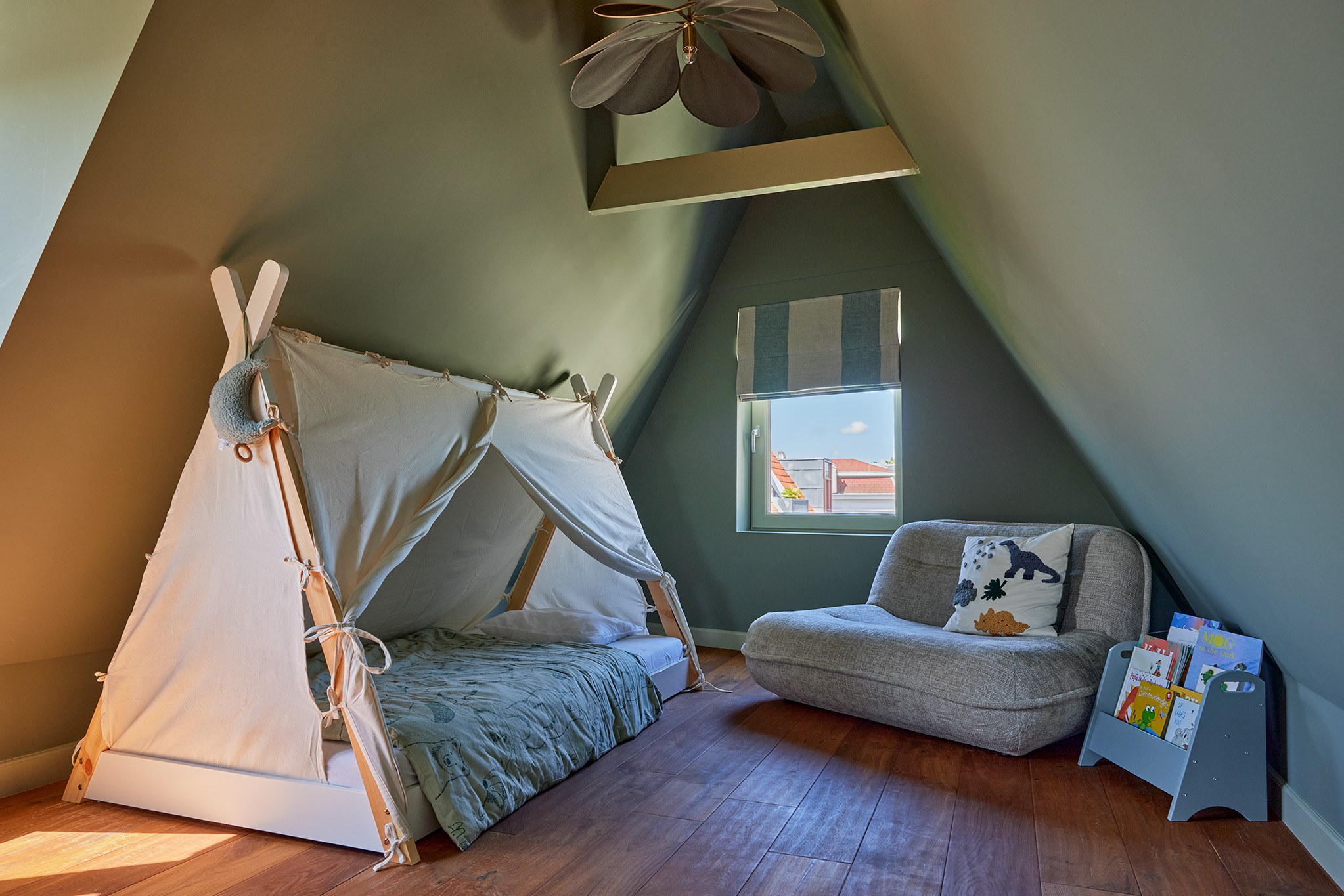 Kinderkamer onder schuin dak met olijfgroene wanden, tipi-bed en grijze fauteuil.