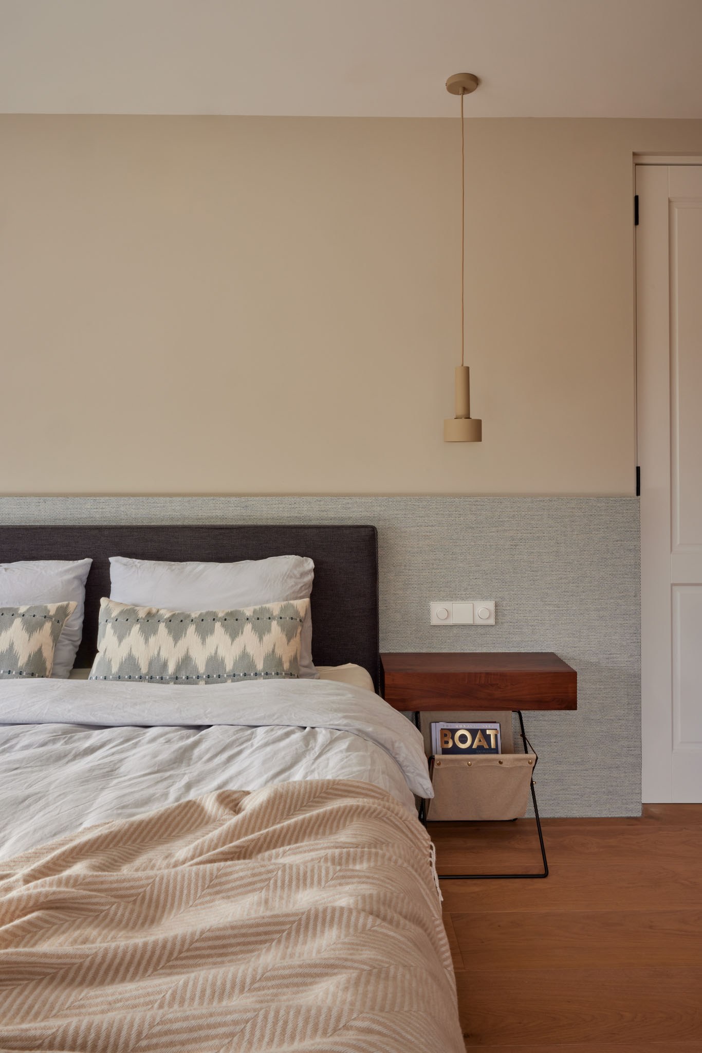 Rustige slaapkamer met grijs bed, houten hoofdbord, beige textiel en hanglamp.
