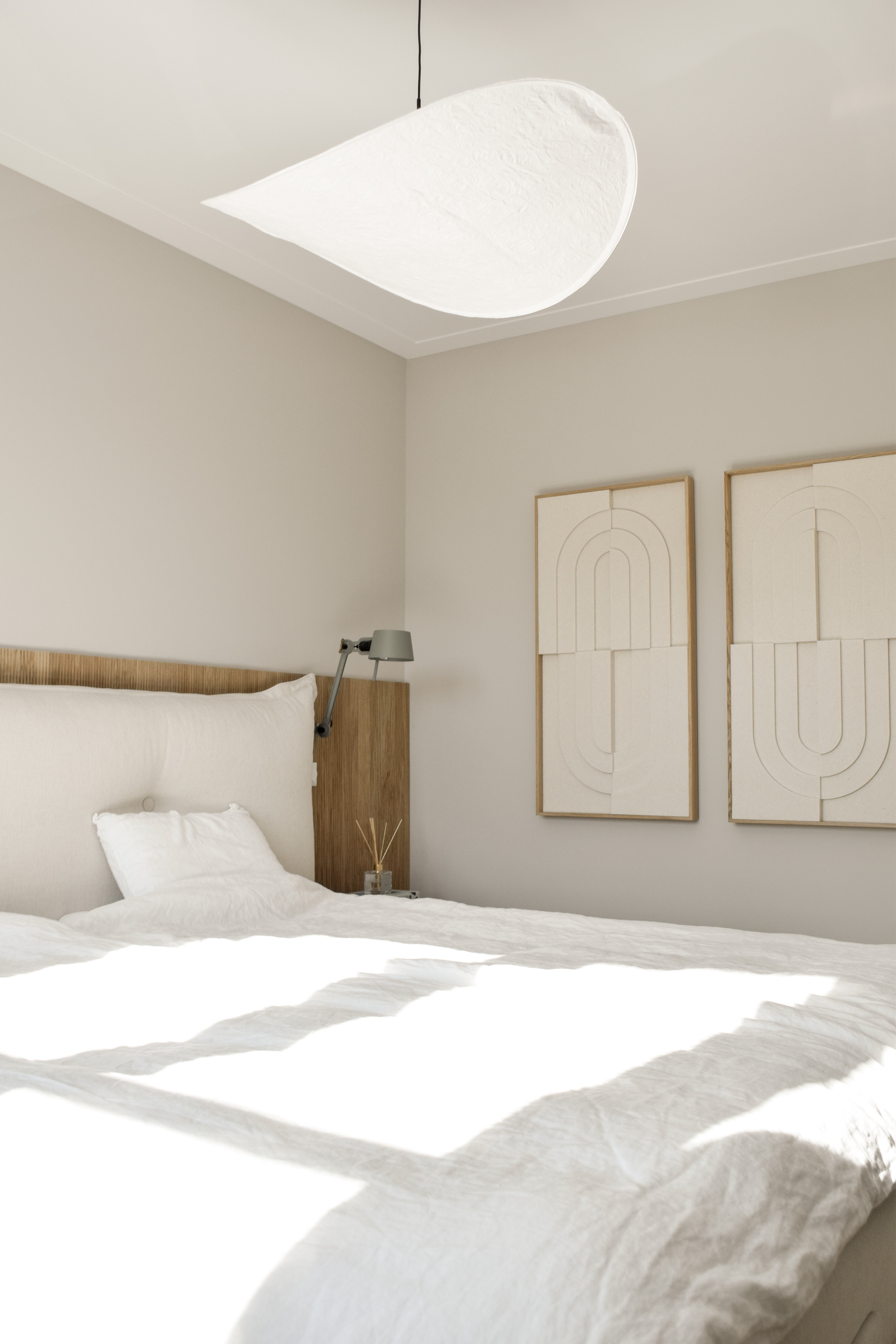 Rustige slaapkamer met eiken hoofdbord, beige-grijze kleuren en sculpturale witte hanglamp.