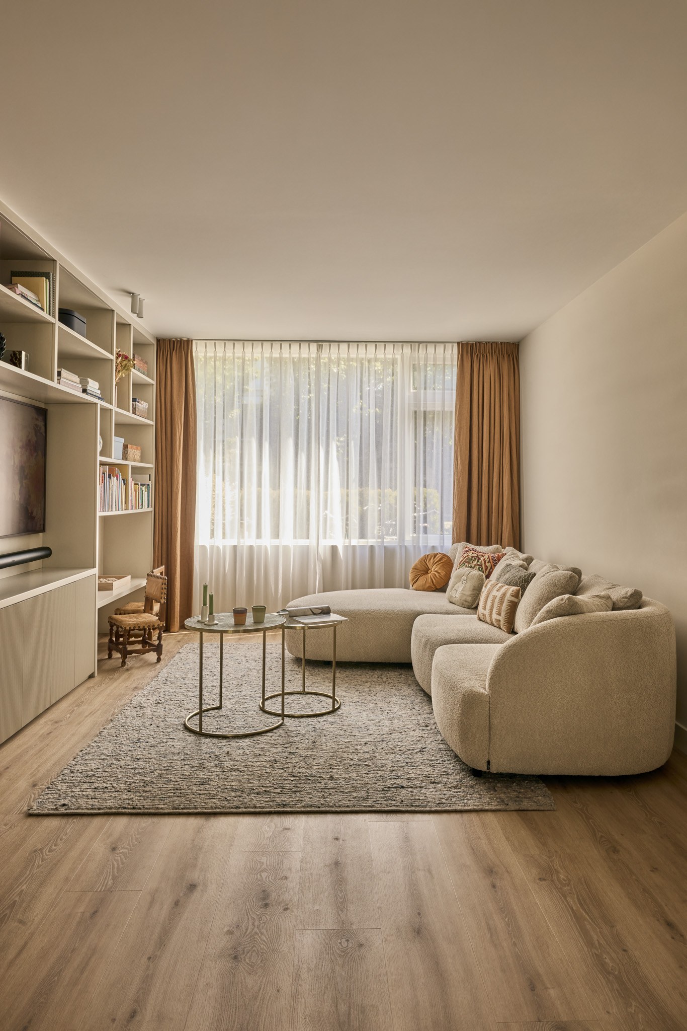 Warme neutrale woonkamer met crèmekleurige organische hoekbank, beige maatwerkwand en houtlook vloer.
