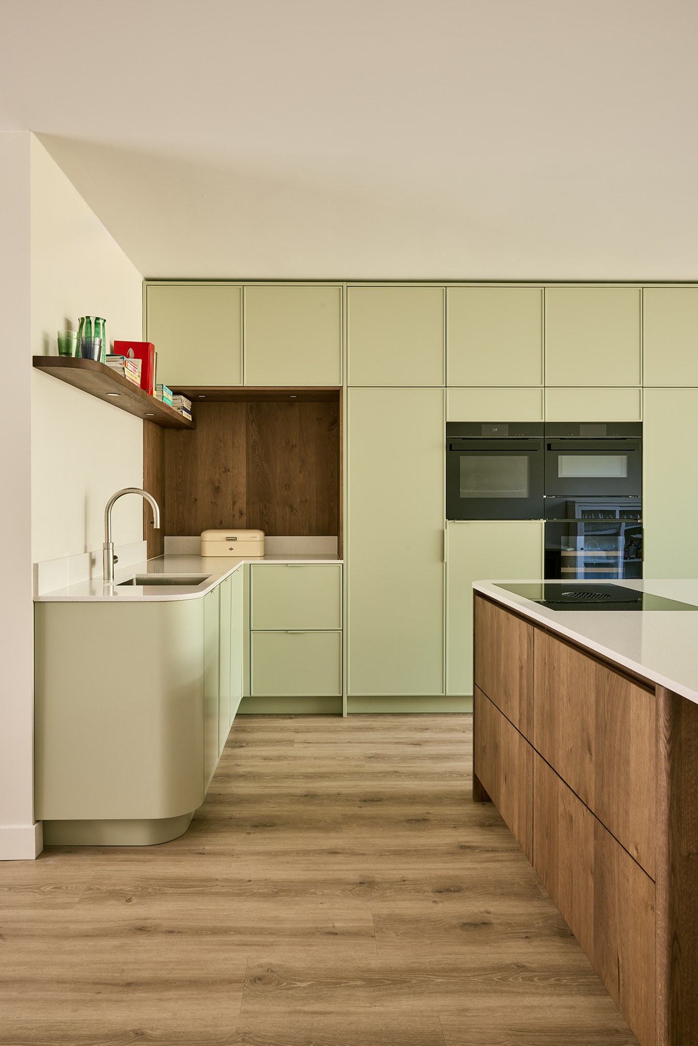 Open keuken met saliegroene kastenwand, eiken eiland en licht natuurstenen werkblad.
