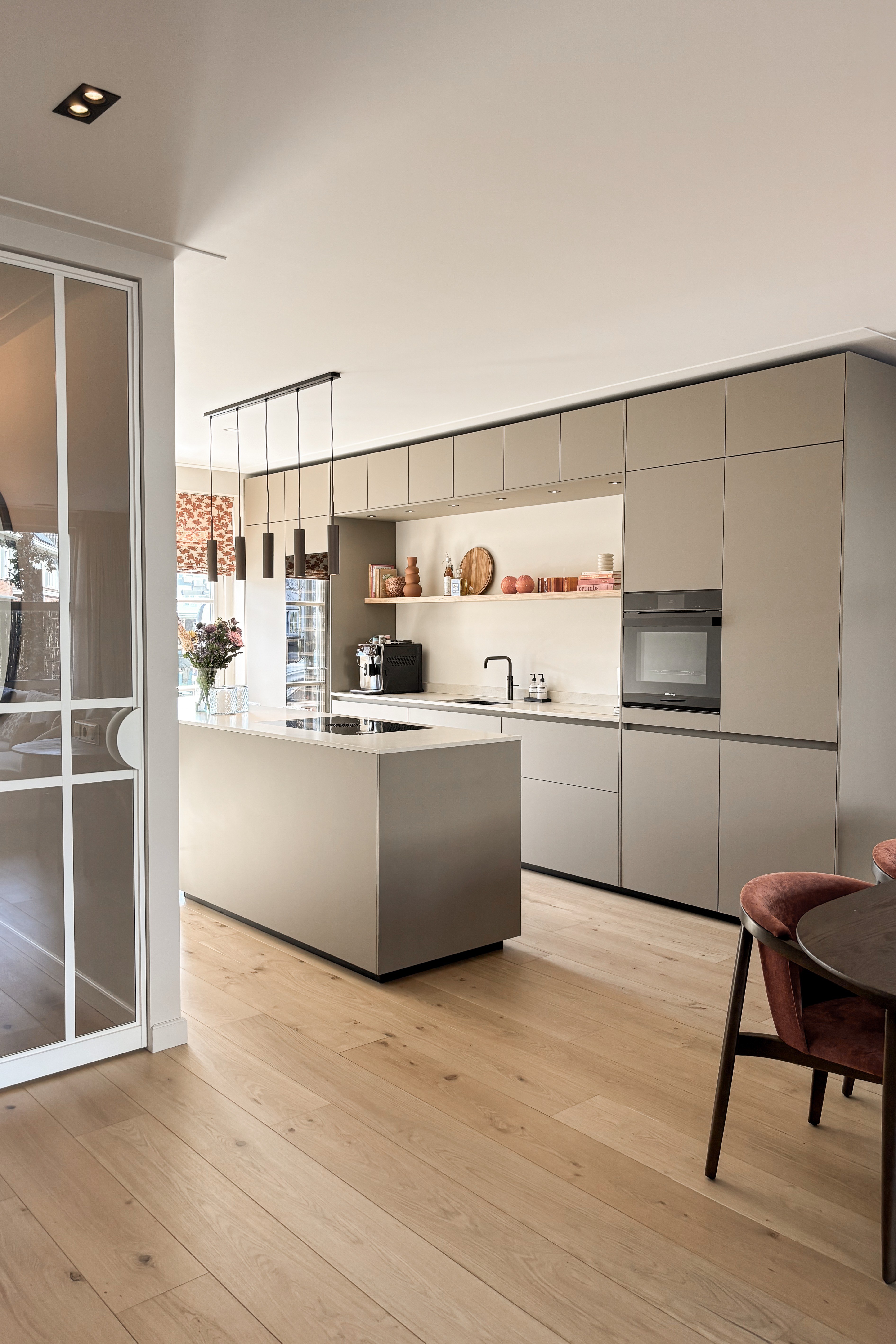 Brede taupe maatwerkkeuken met kookeiland en warme houten vloer.