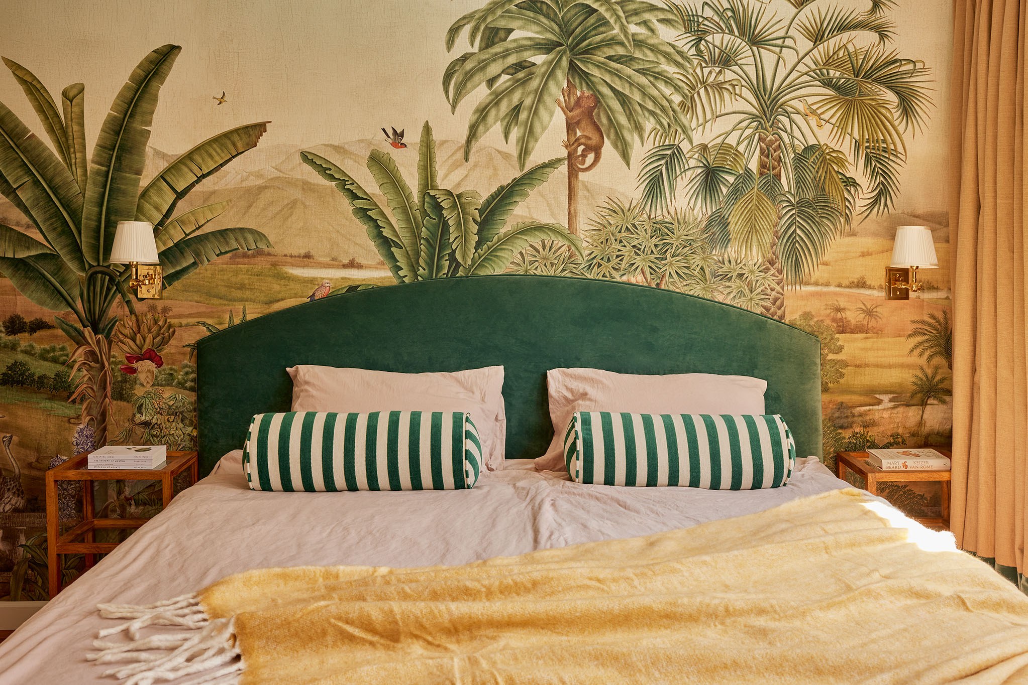 Tropische slaapkamer met panoramische junglemuurschildering, emeraldgroen hoofdbord en gele plaid.