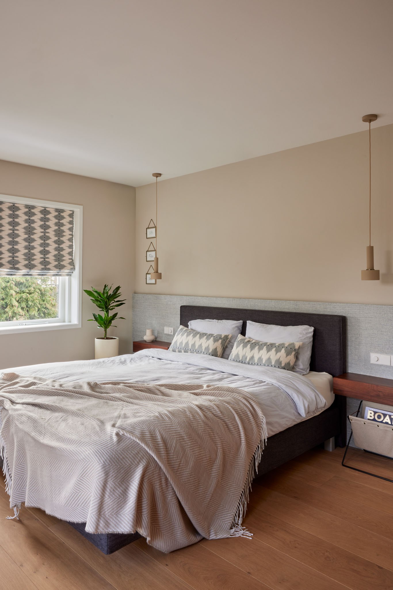 Neutrale slaapkamer met houten hoofdbord, grijs bed en grafische vouwgordijnen.