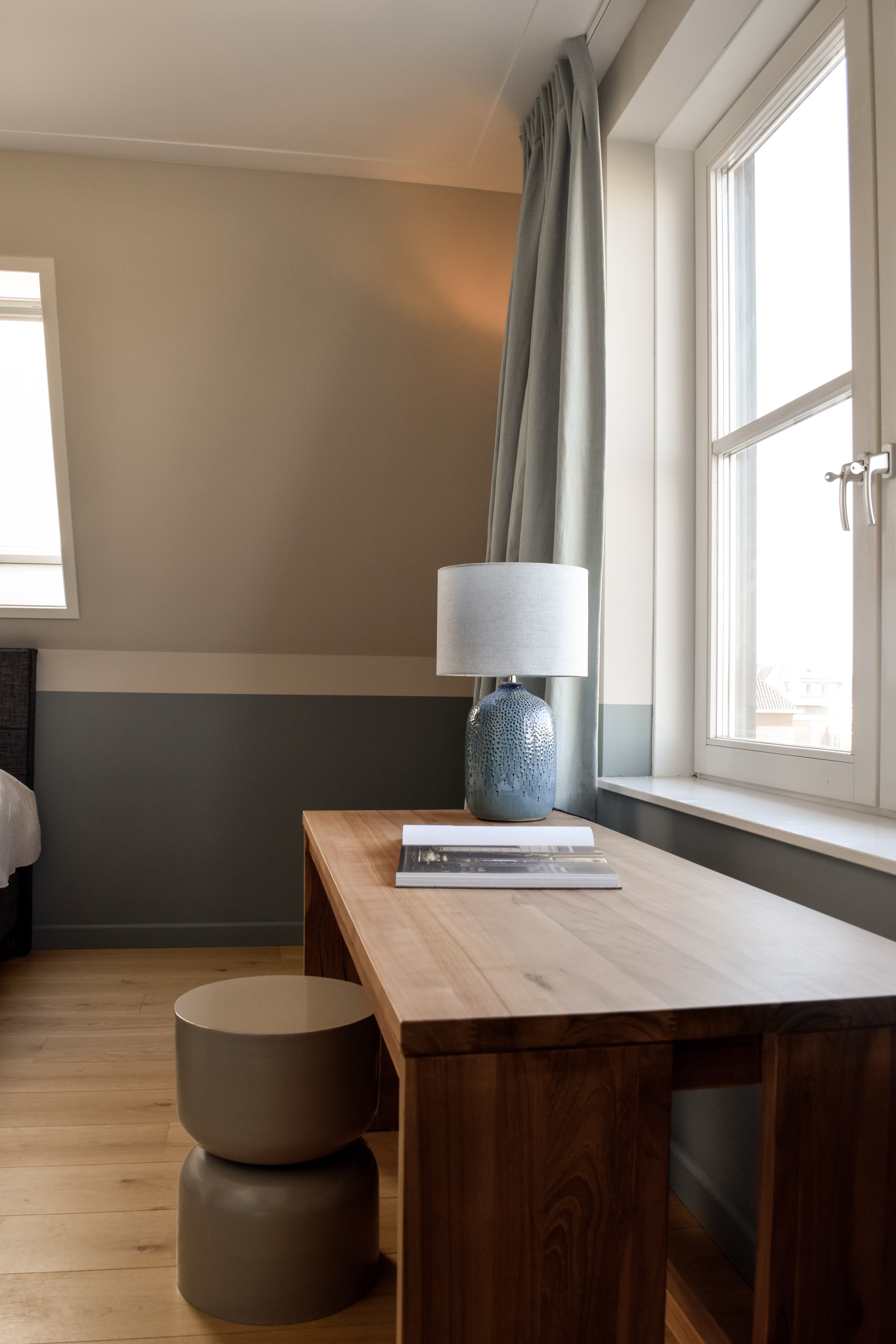 Compact thuiskantoor met houten werkblad onder het raam en blauwgrijze wand.