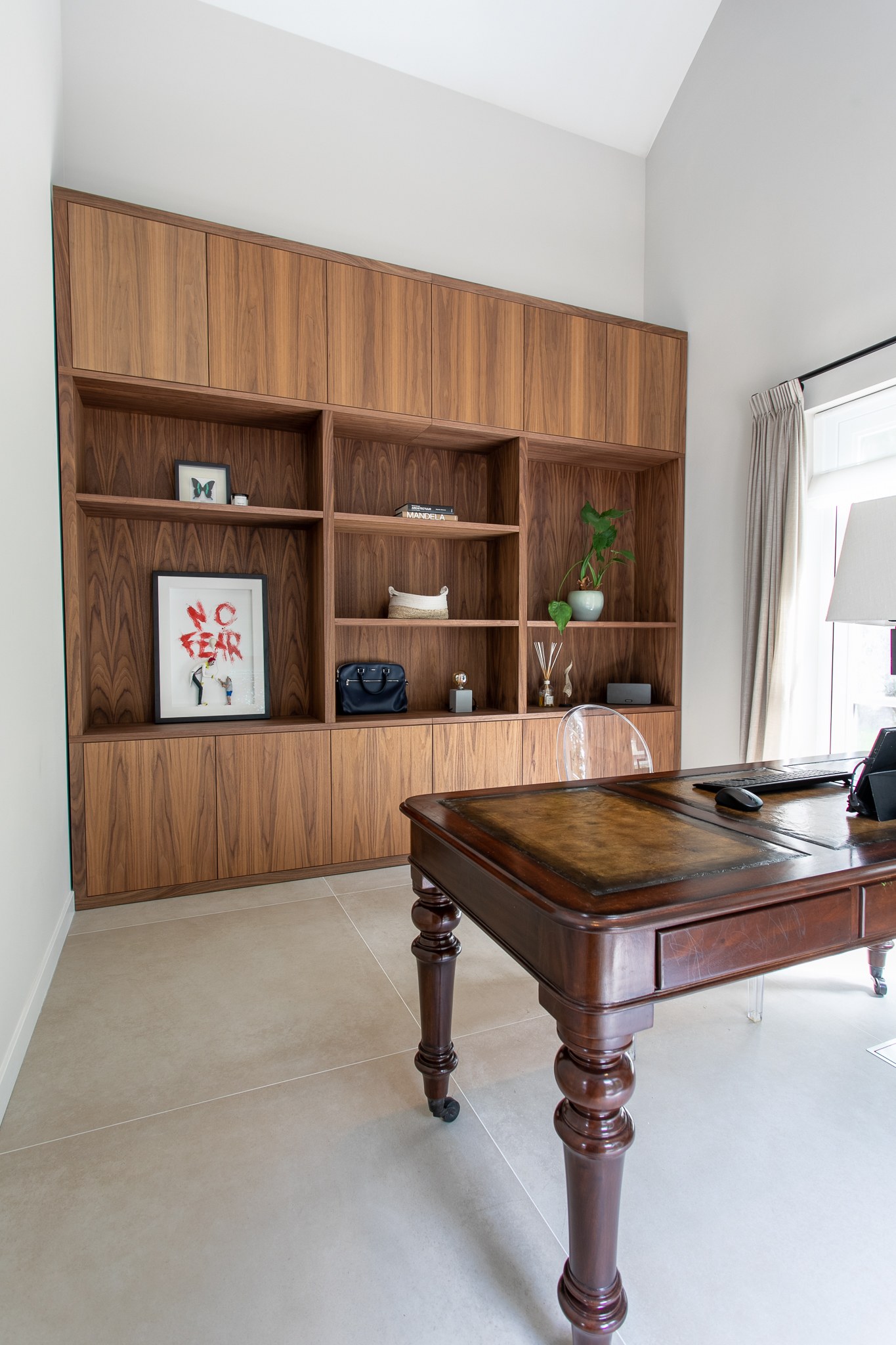 Licht thuiskantoor met kamerhoge walnoot maatwerkkast en open vakken, klassiek houten bureau, lichte vloer en witte wanden.
