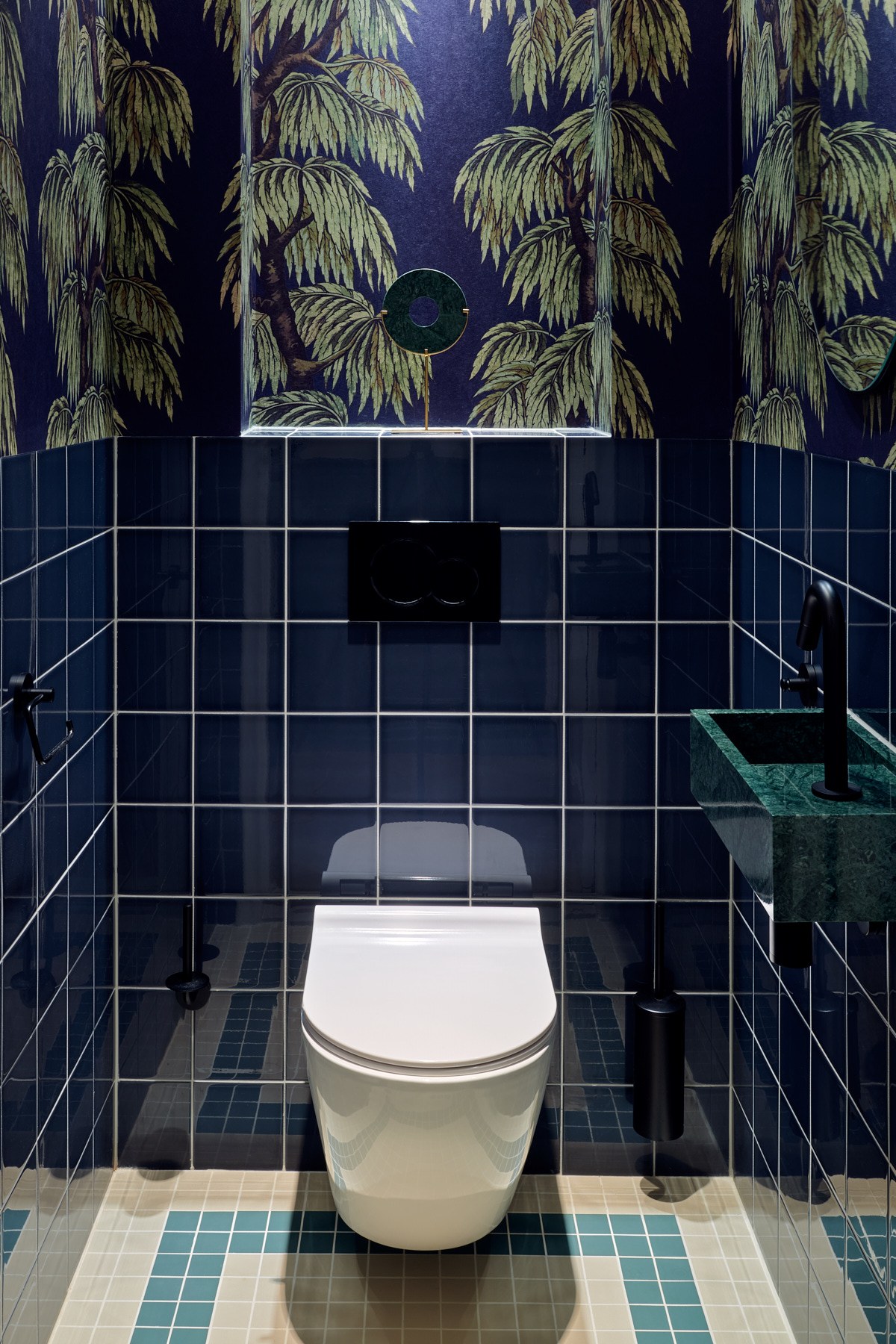 Uitgesproken toiletruimte in Bussum met glanzende donkerblauwe tegels, botanisch behang, groen marmeren fontein en zwarte en messing details.