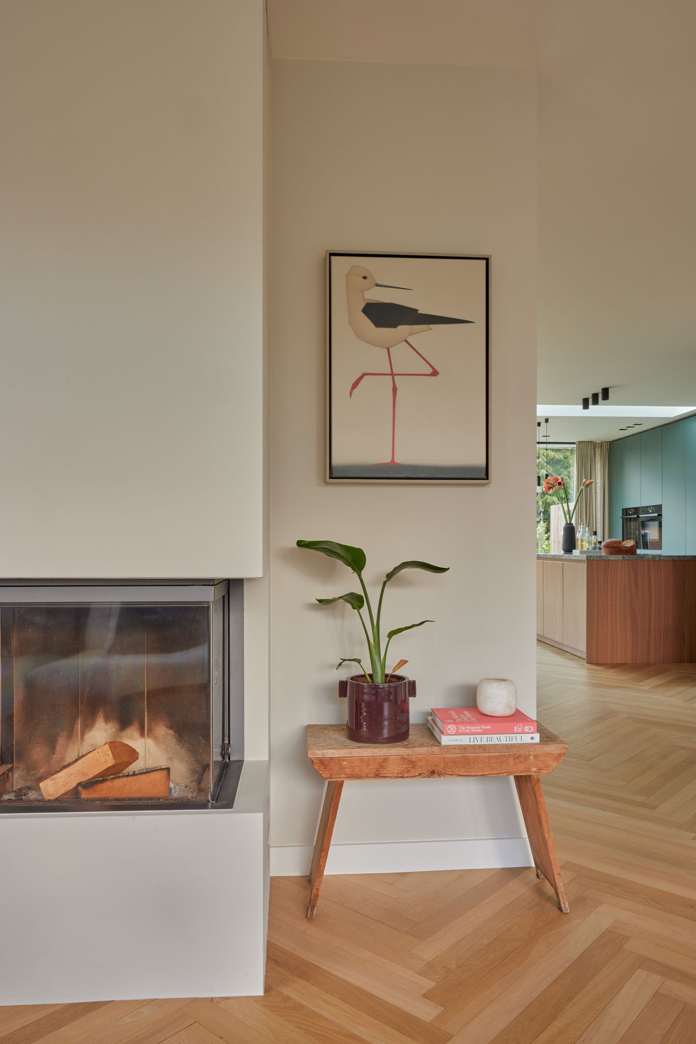 Lichte woonkamer met driezijdige haard, visgraatvloer en zachte neutrale kleuren.